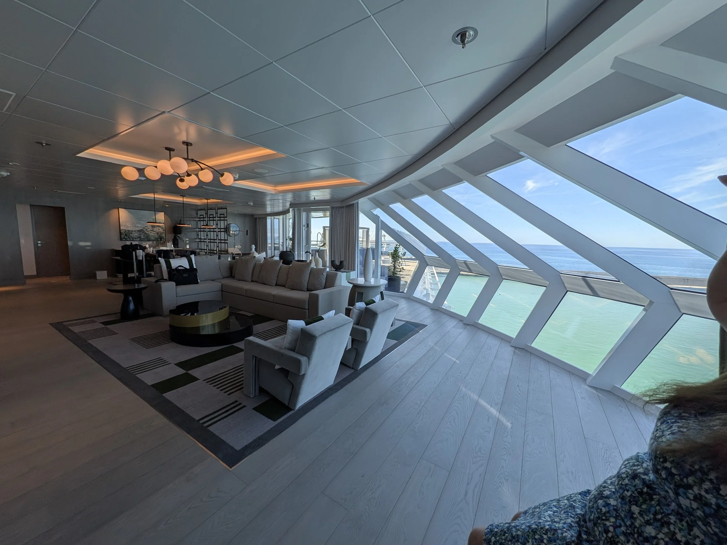 Celebrity suite living room with sweeping angled floor-to-ceiling ocean-view windows