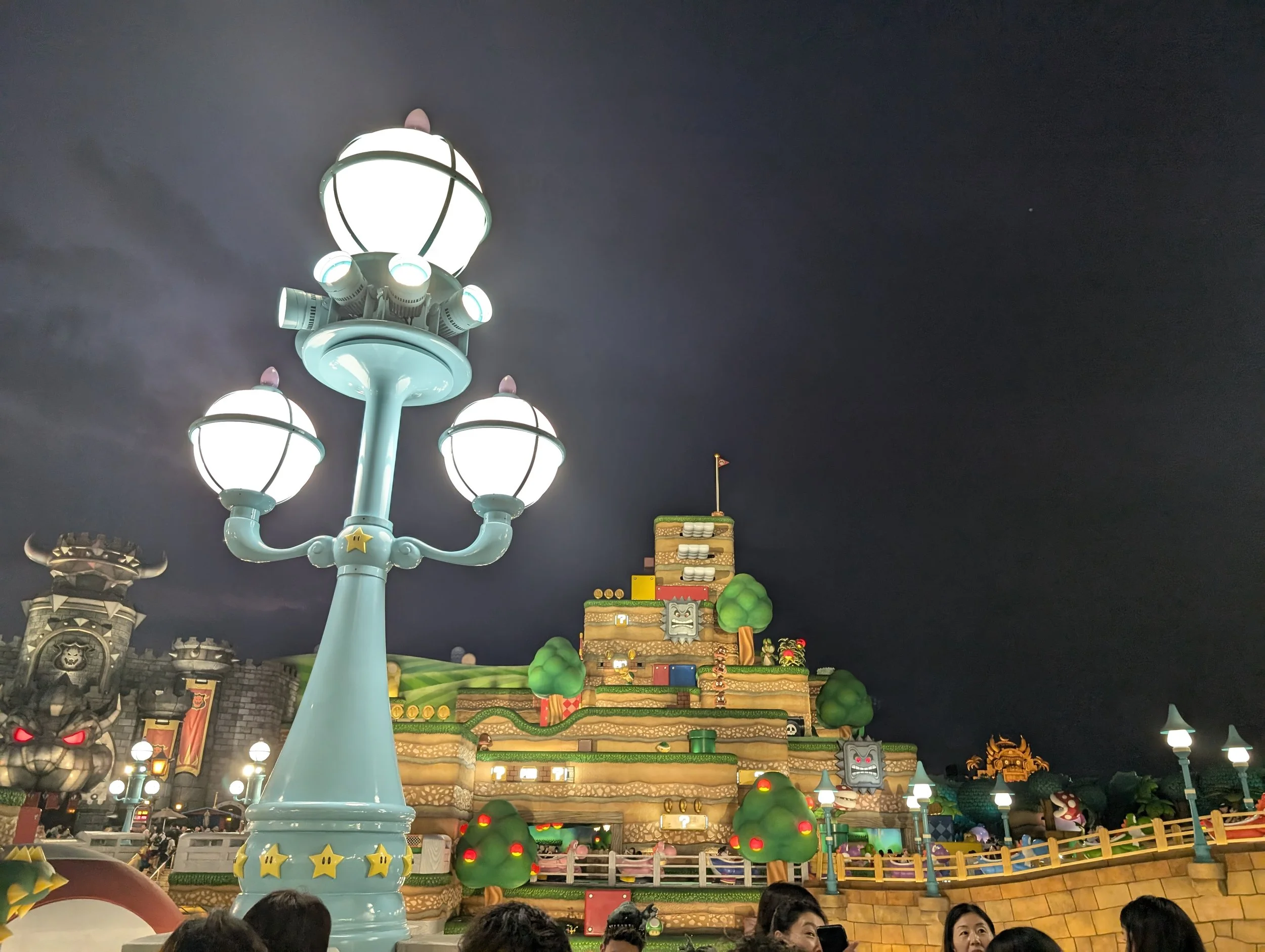 Super Nintendo World lit up at night with Peach's Castle and Mushroom Kingdom lamp posts at Universal Studios Japan