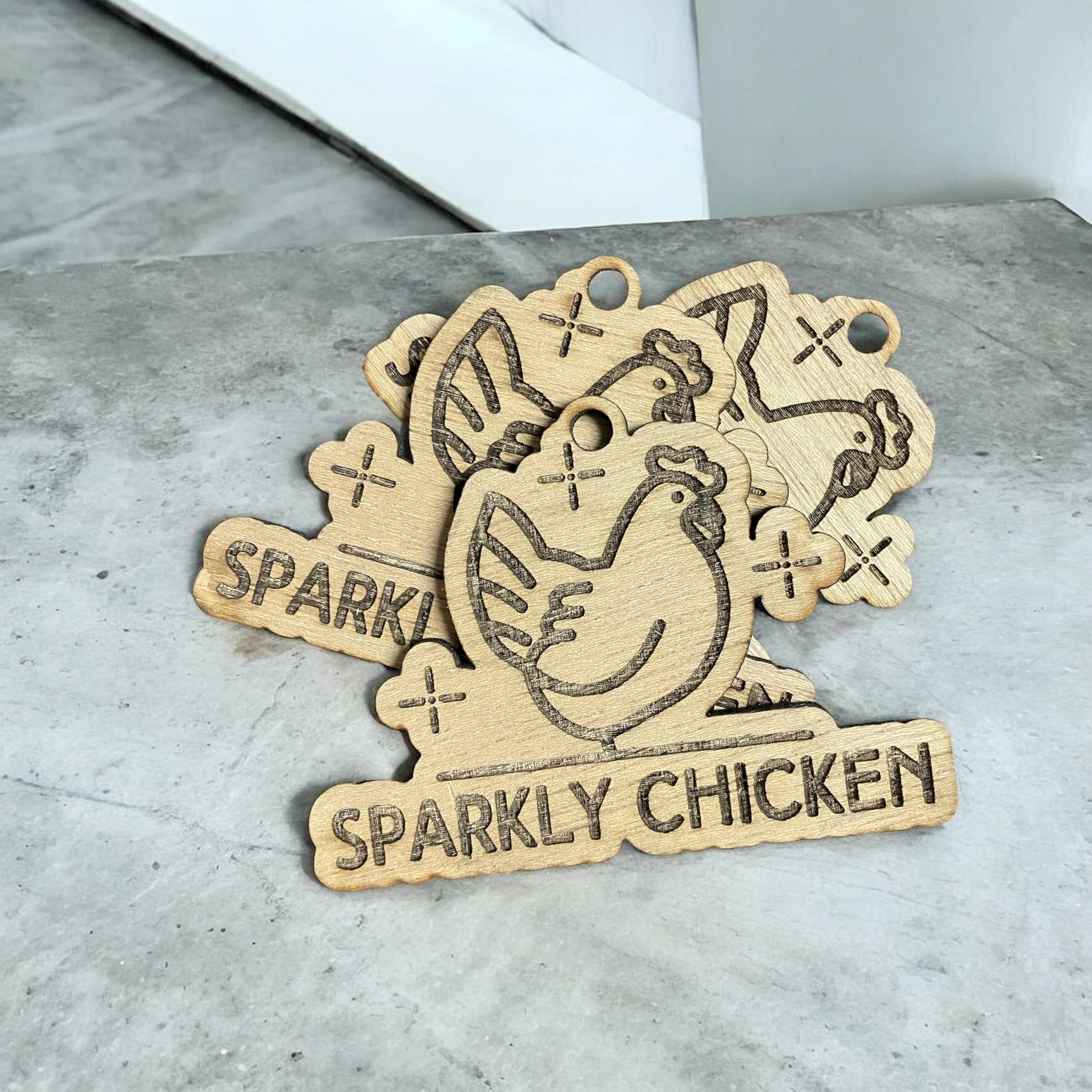 Wooden tags featuring a chicken illustration and the text 'Sparkly Chicken' on a gray surface.