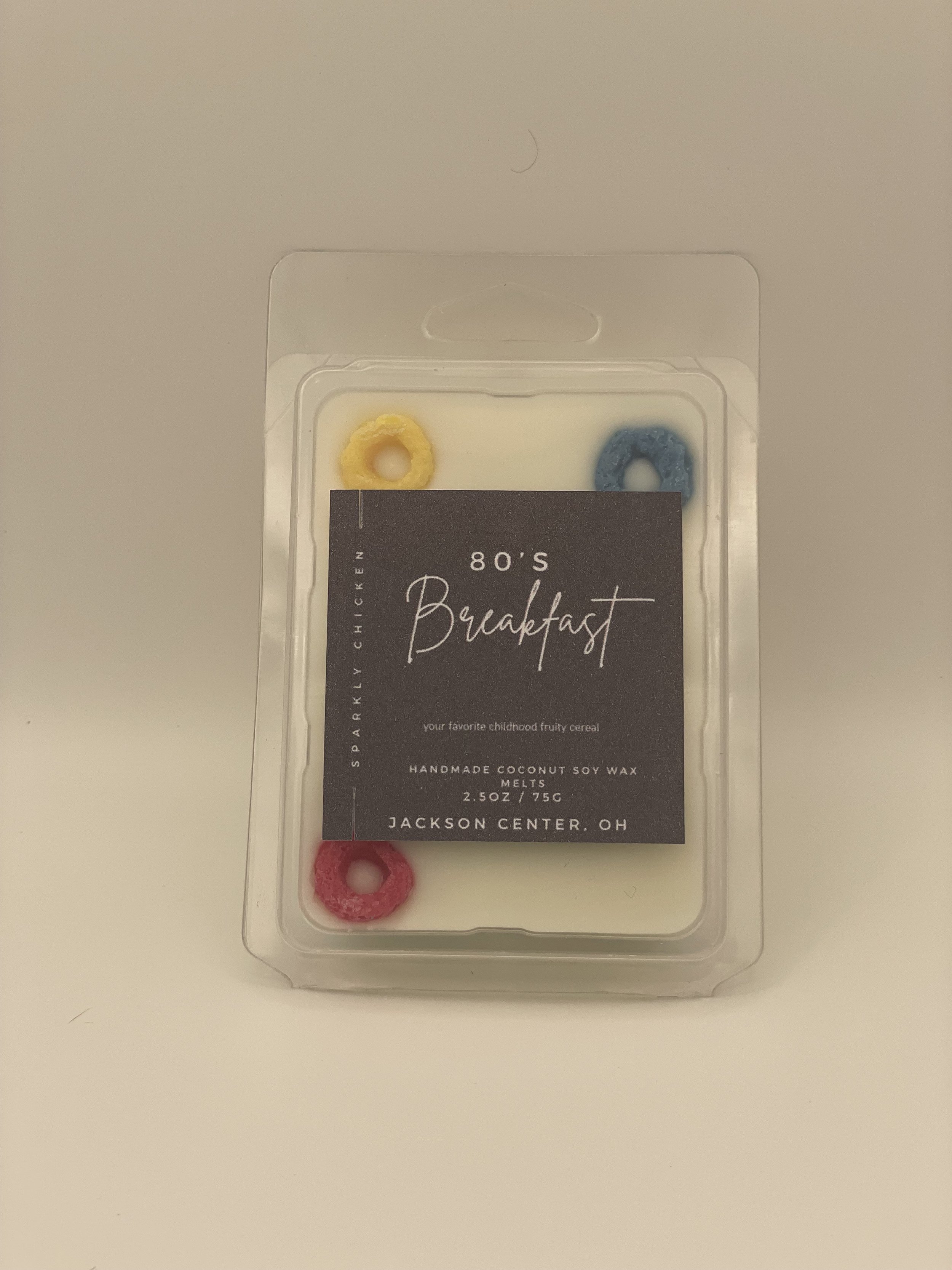 Packaging of a candle with colorful cereal-shaped wax melts labeled '80's Breakfast' from Jackson Center, Ohio, featuring yellow, blue, and red wax melts.
