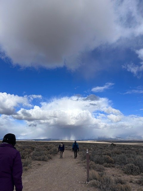 People walking on West Rim trail through a desert landscape with rain squall in distance.