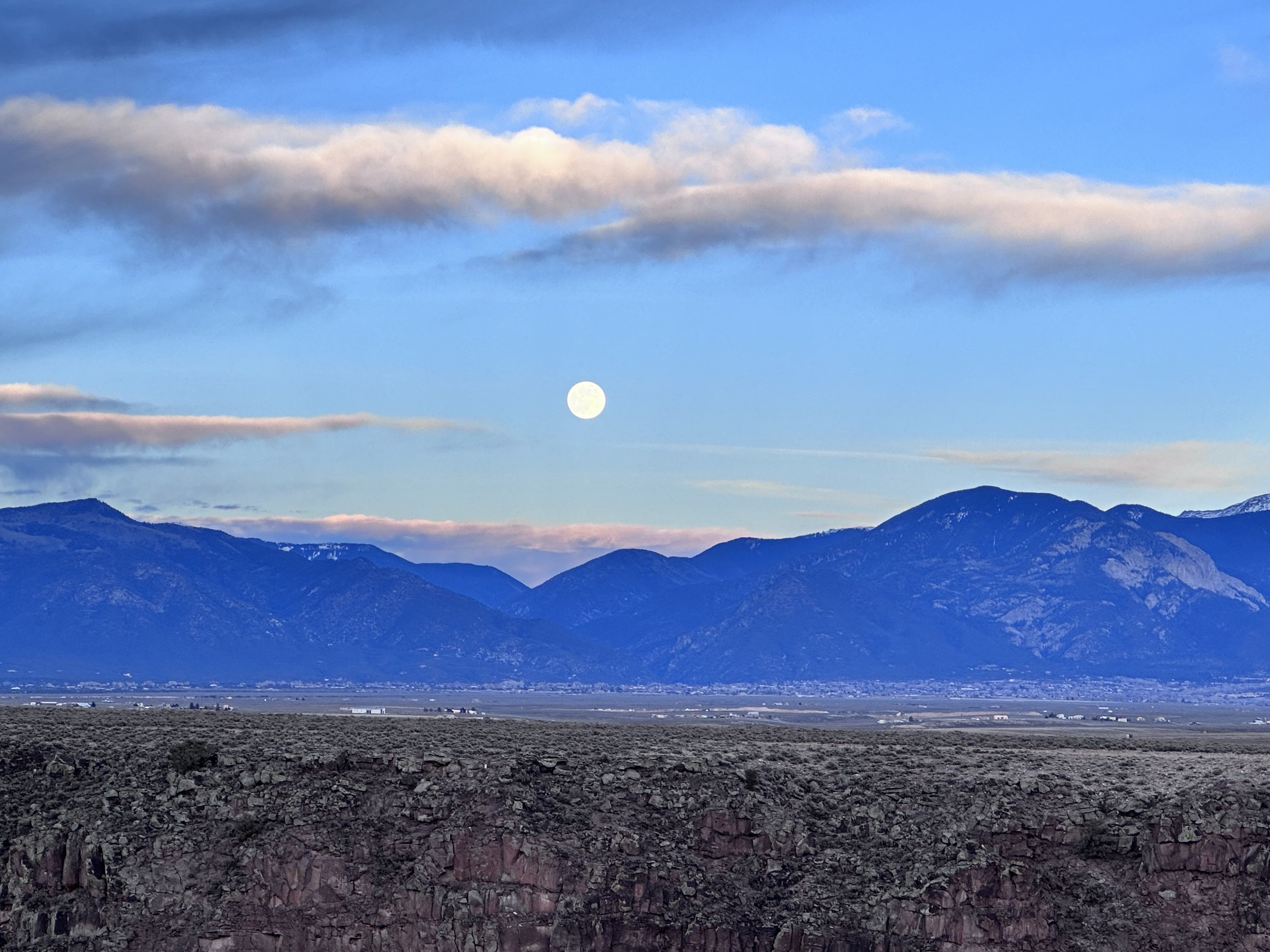 Full moon over a Sangre De Cristos mountain range with scattered clouds at sunset.