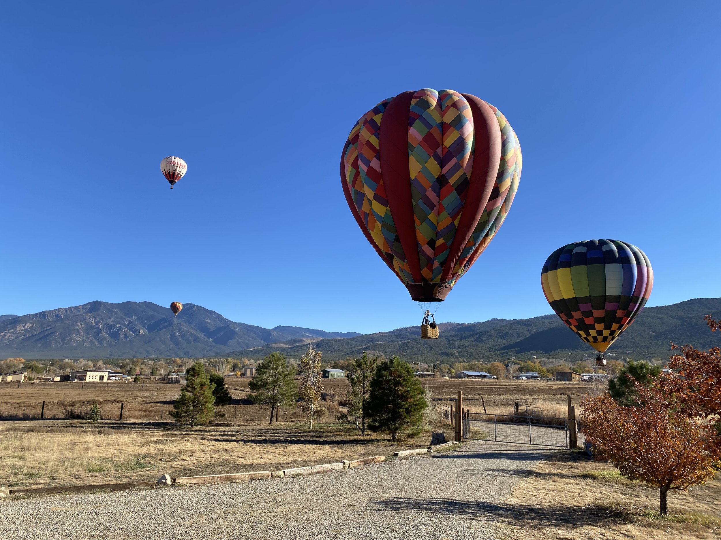 Taos hot air balloon festival held in October each year, floating over a rural field with mountains in the background under a clear blue sky.