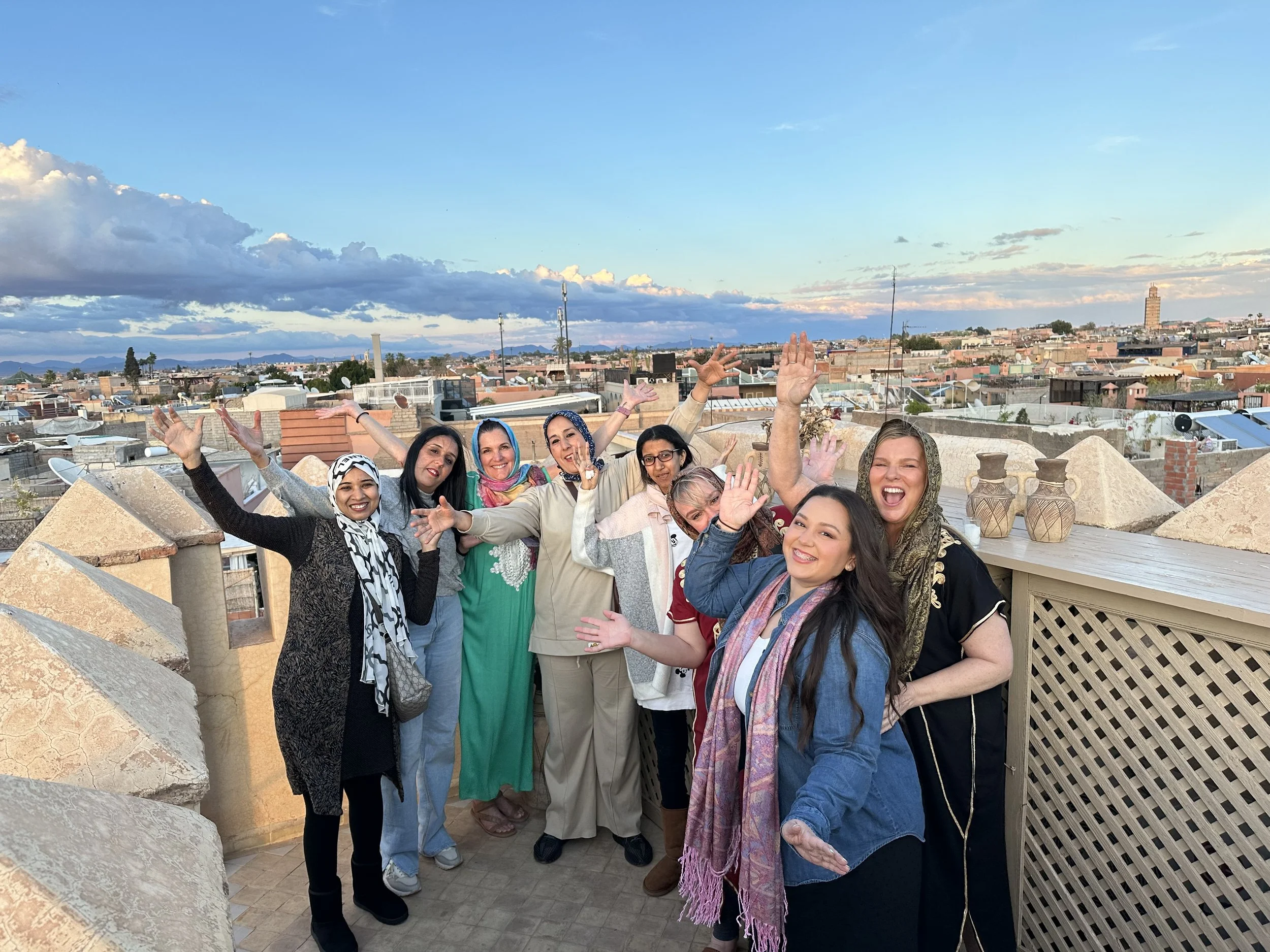 Group of happy women celebrating on rooftop with cityscape and sunset sky in the background.