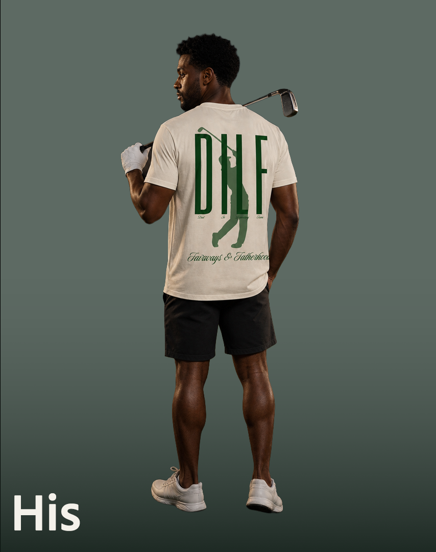 A man standing with his back to the camera, holding a golf club over his shoulder. He is shirtless underneath a white t-shirt with a large green print and text that reads "DNL" and "Fairways & Fatherhood." He is wearing black shorts, white shoes, and appears to be ready for a round of golf. The background is plain and gray.