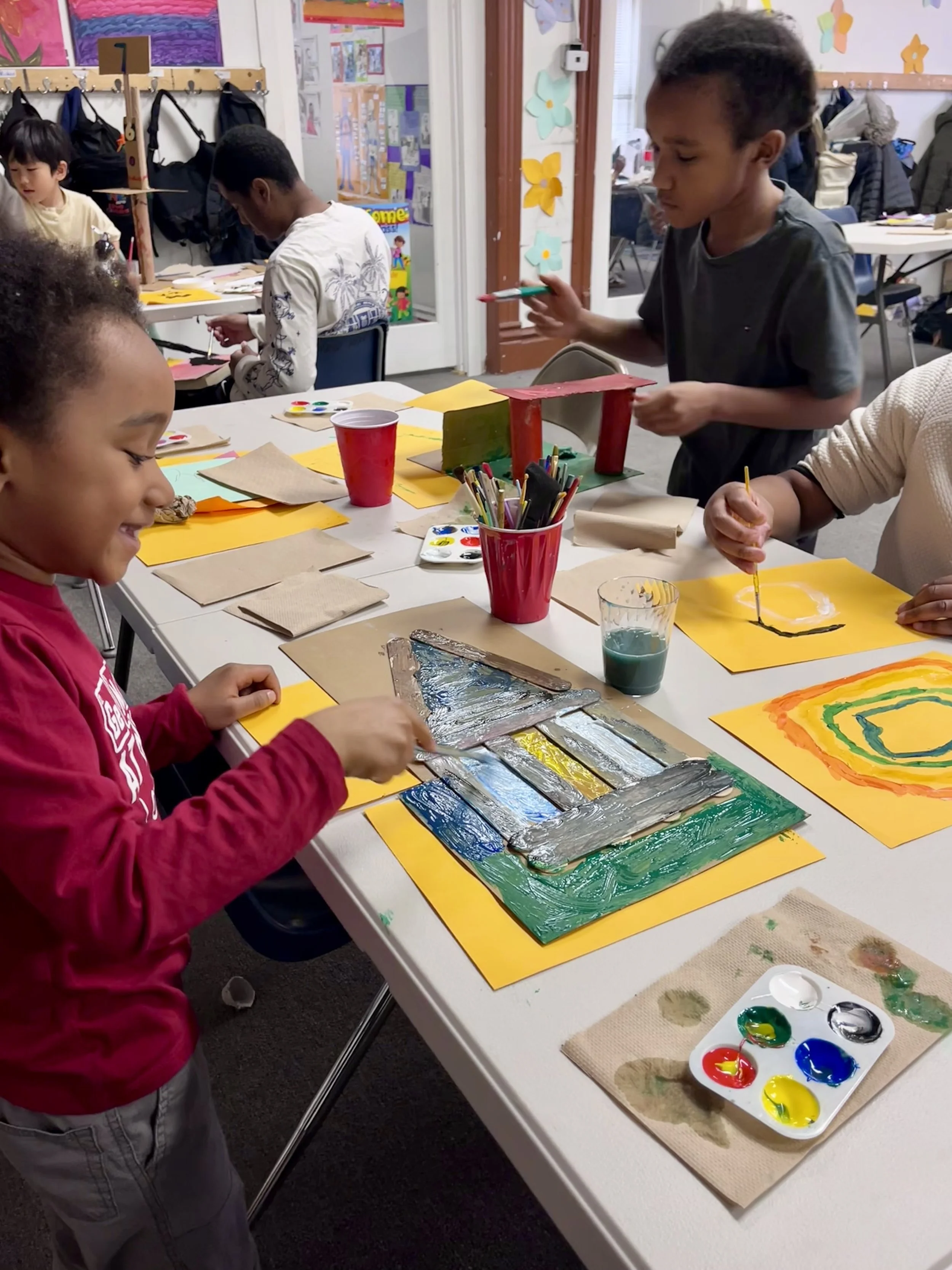 Children engaged in an art activity, painting on paper with bright colors in a classroom.