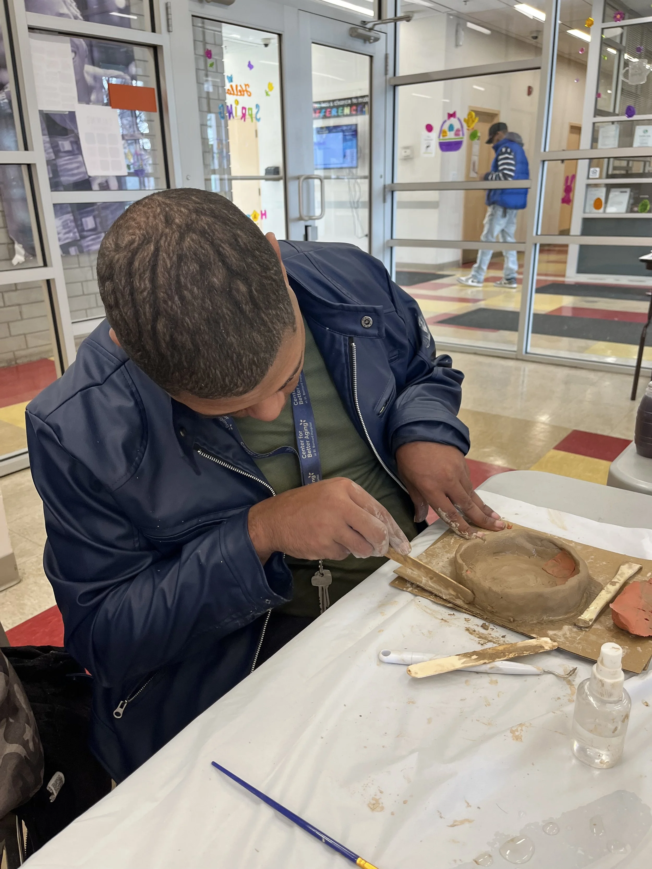 A man working on a ceramic project at a table in a classroom or workshop.