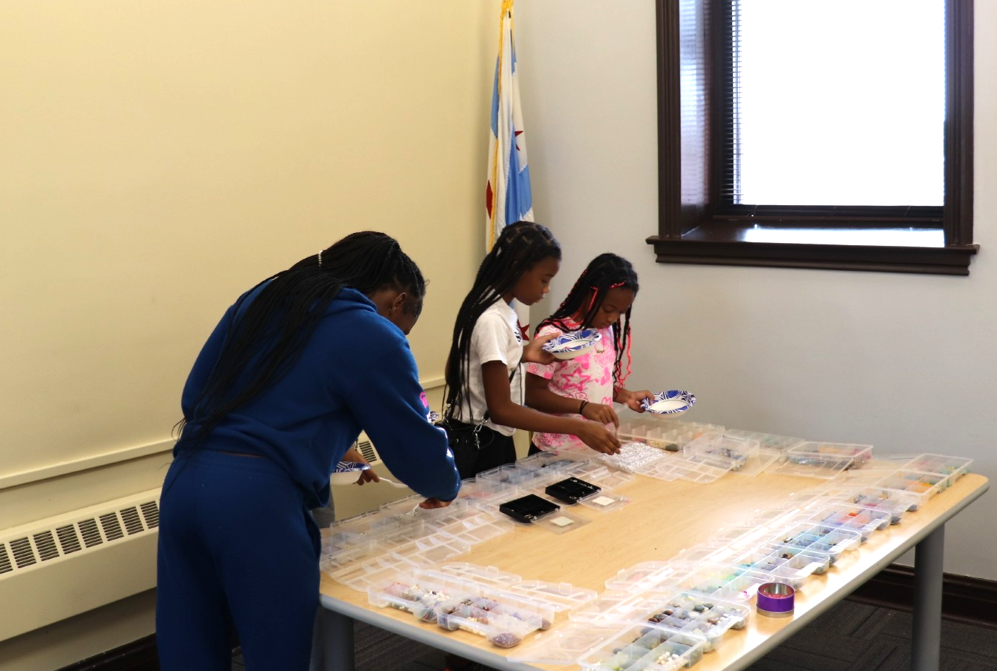Four girls stand at a table sorting beads or craft supplies in plastic containers.