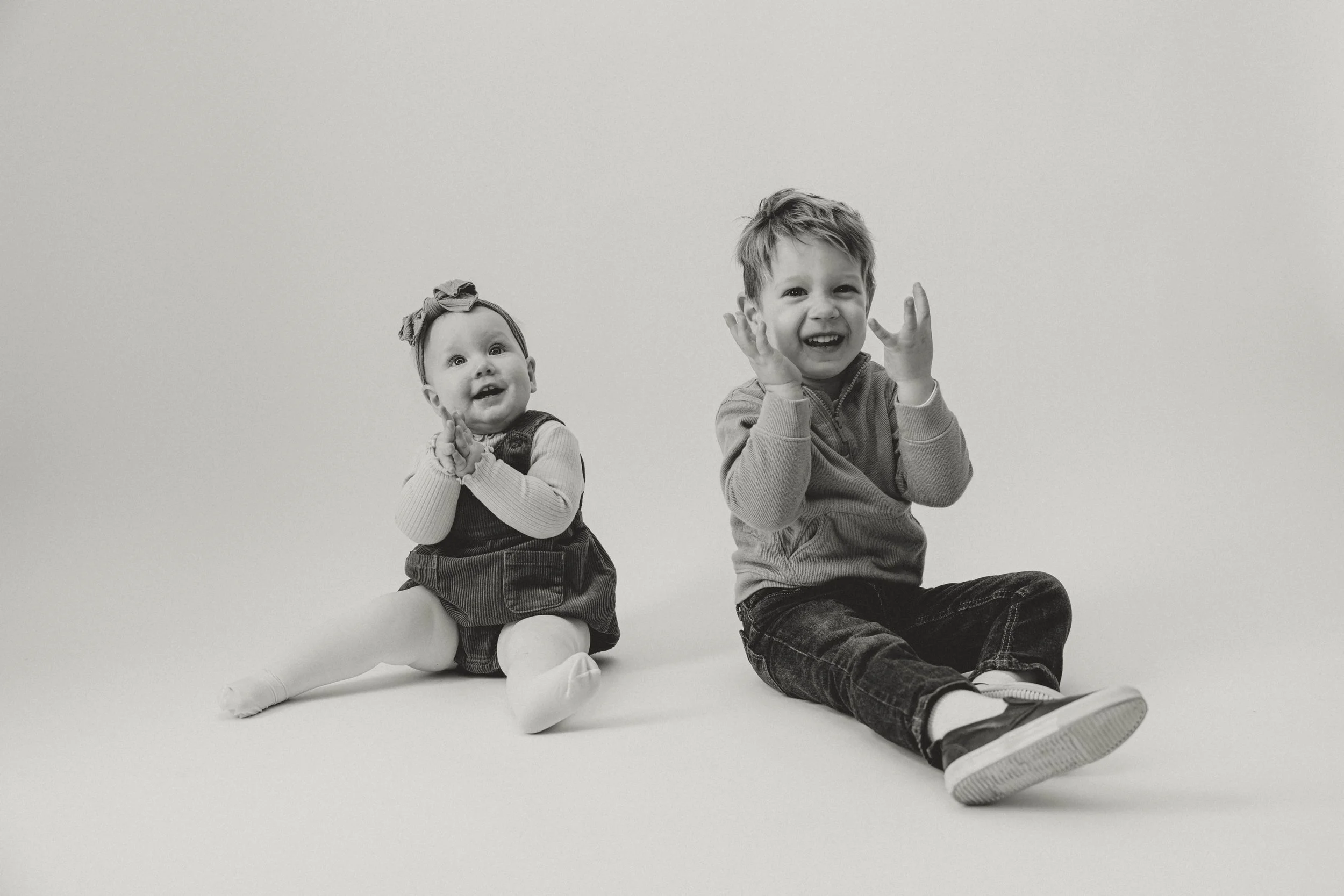 Black and white photo of a young girl and a boy sitting on the floor, smiling and clapping their hands.