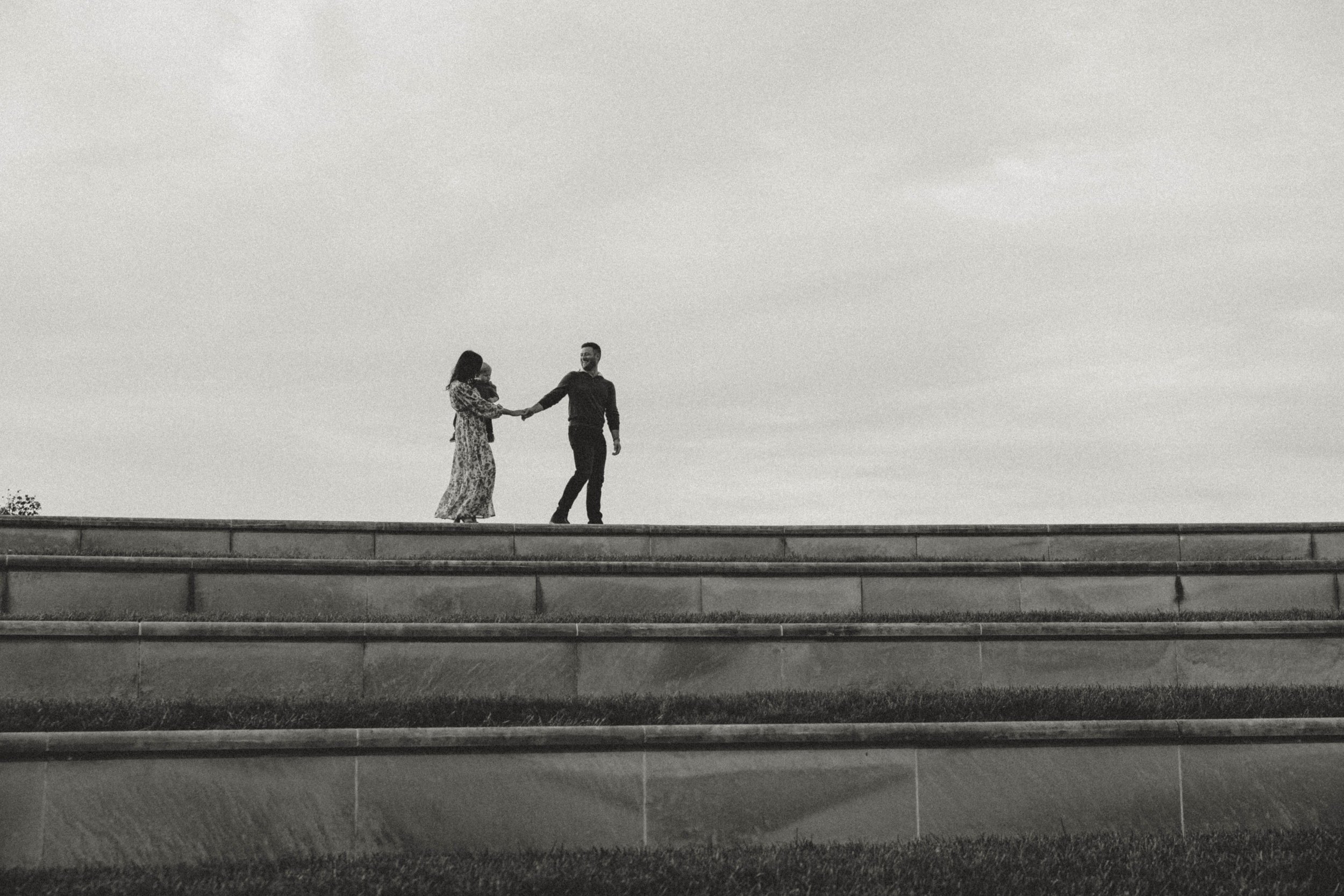 A man and woman holding hands and dancing on a raised platform outdoors, the sky visible in the background.