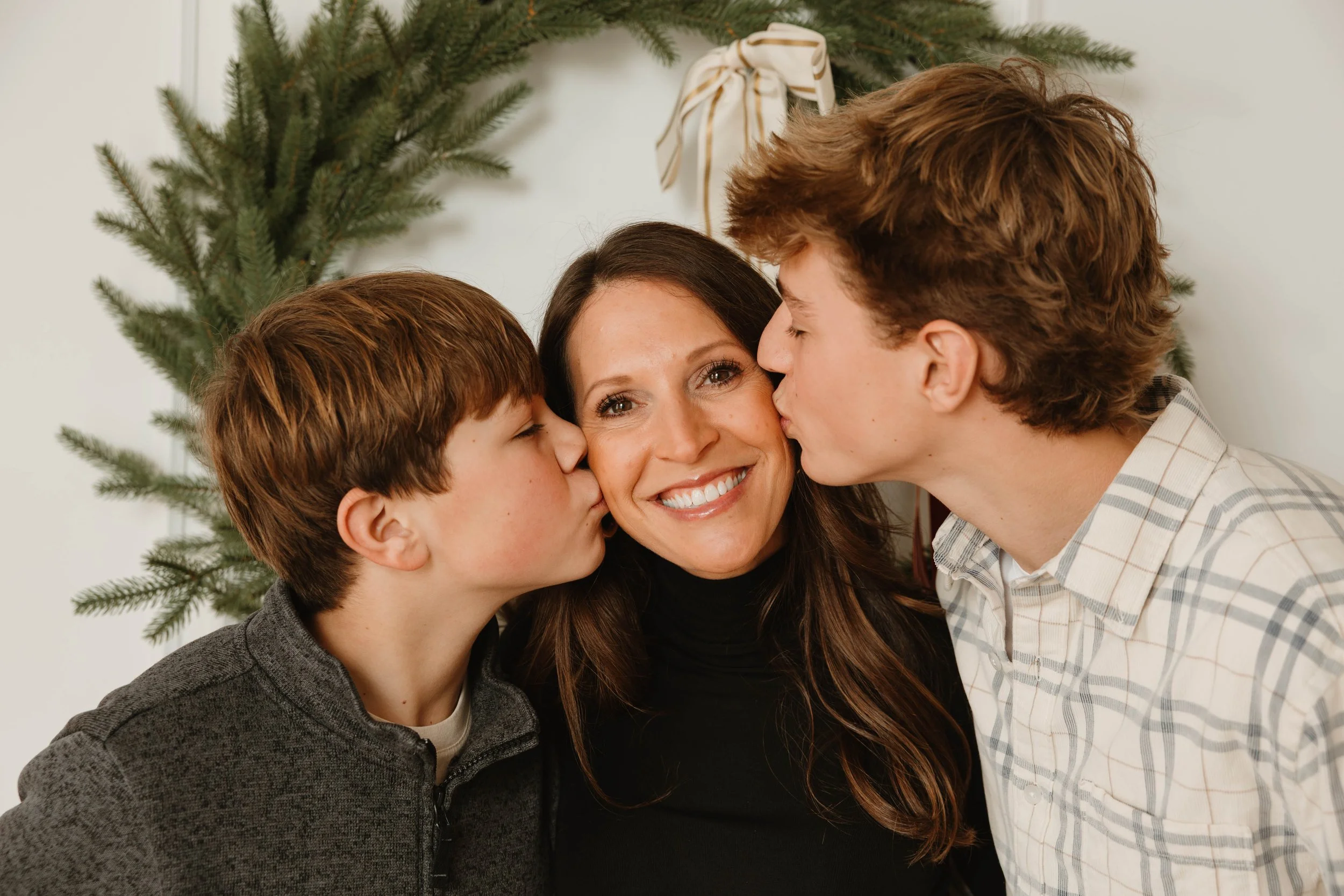 A smiling woman receiving kisses on each cheek from two young boys.