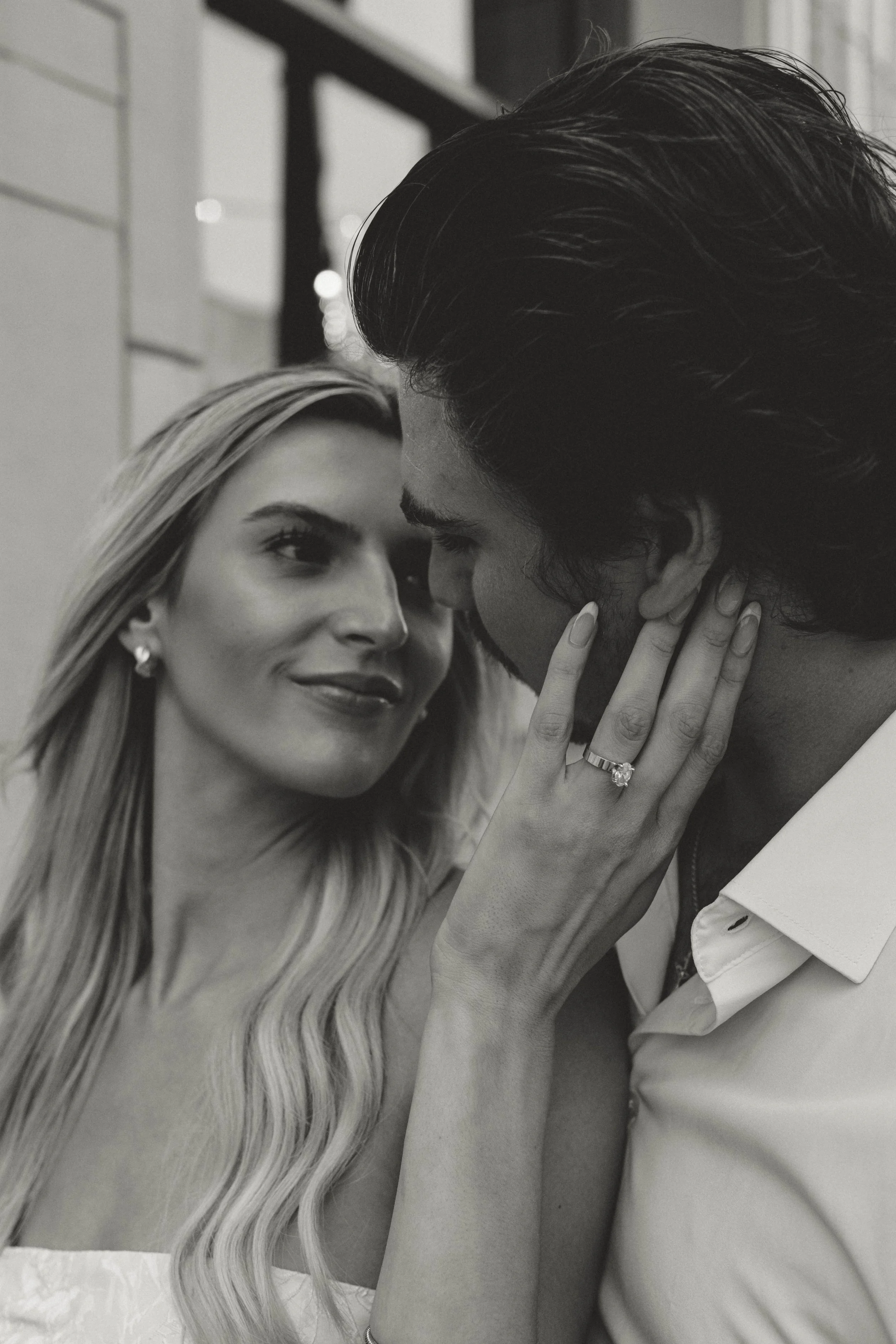 A woman and man close together, holding her face, gazing into each other's eyes, in a black and white photo.