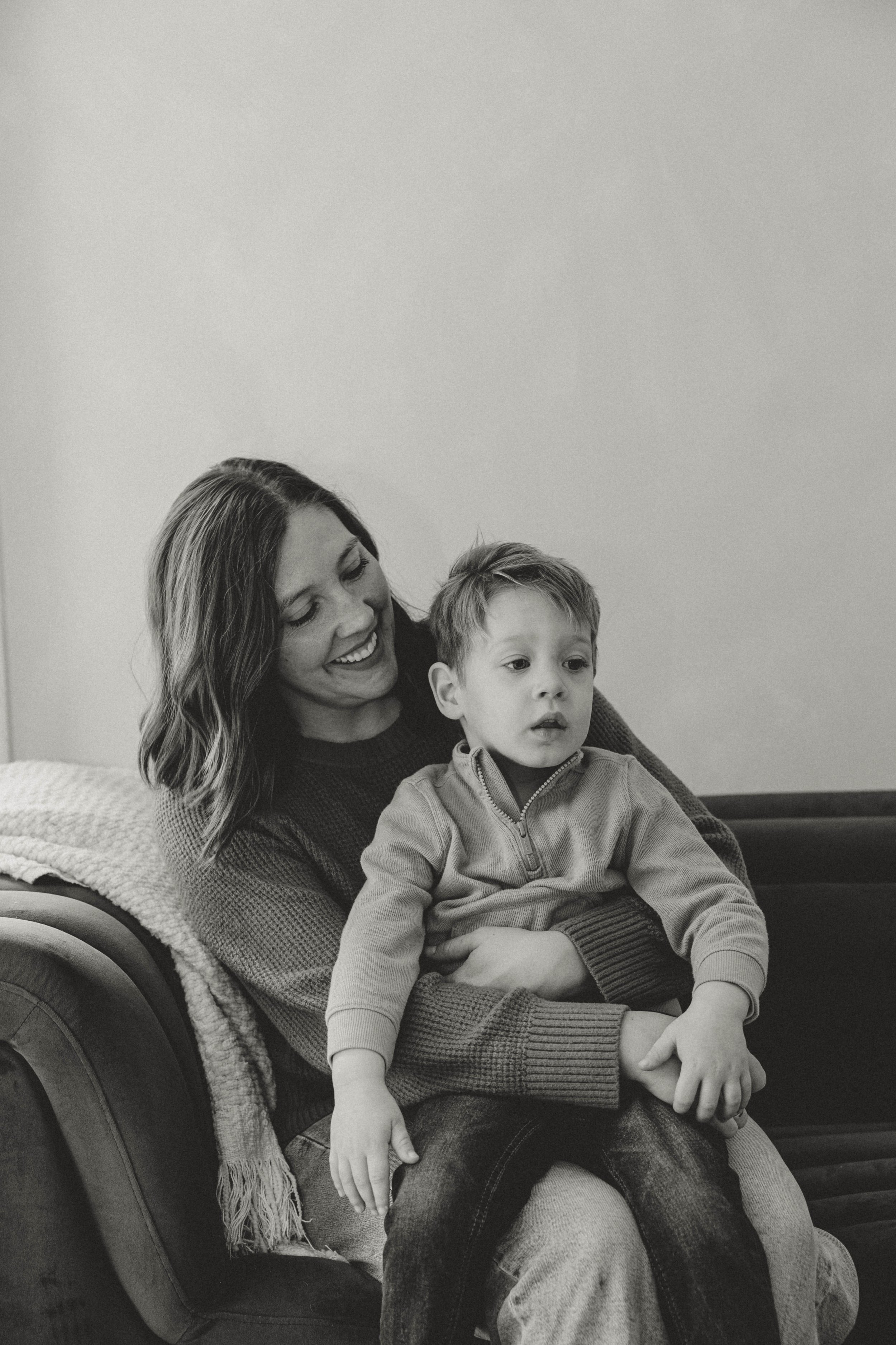A woman and a young boy sitting on a sofa, with the woman smiling and the boy looking away. The photo is in black and white.