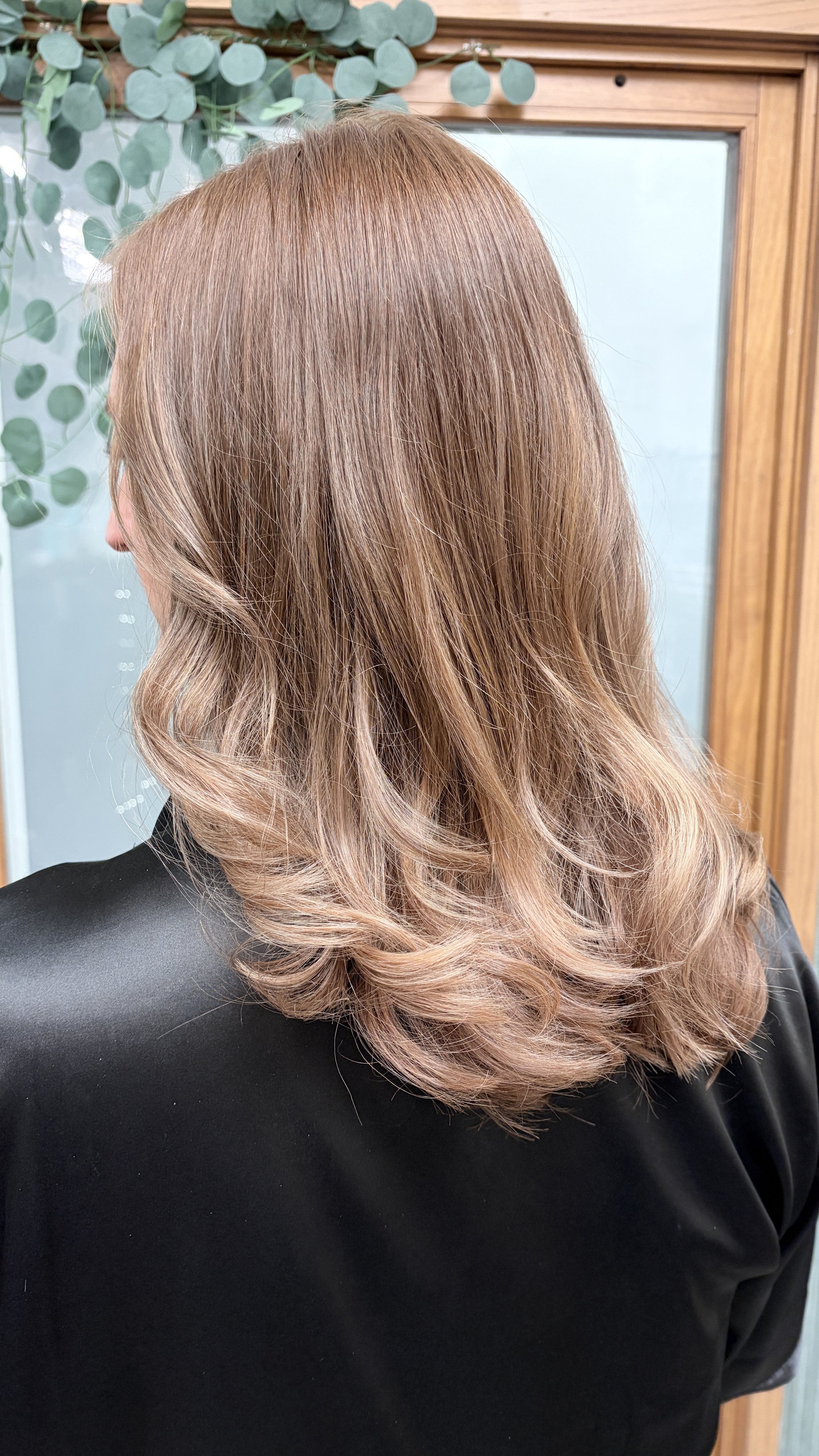 Woman with head turned to left with beige and light brown hair with highlights and curls in her hair.