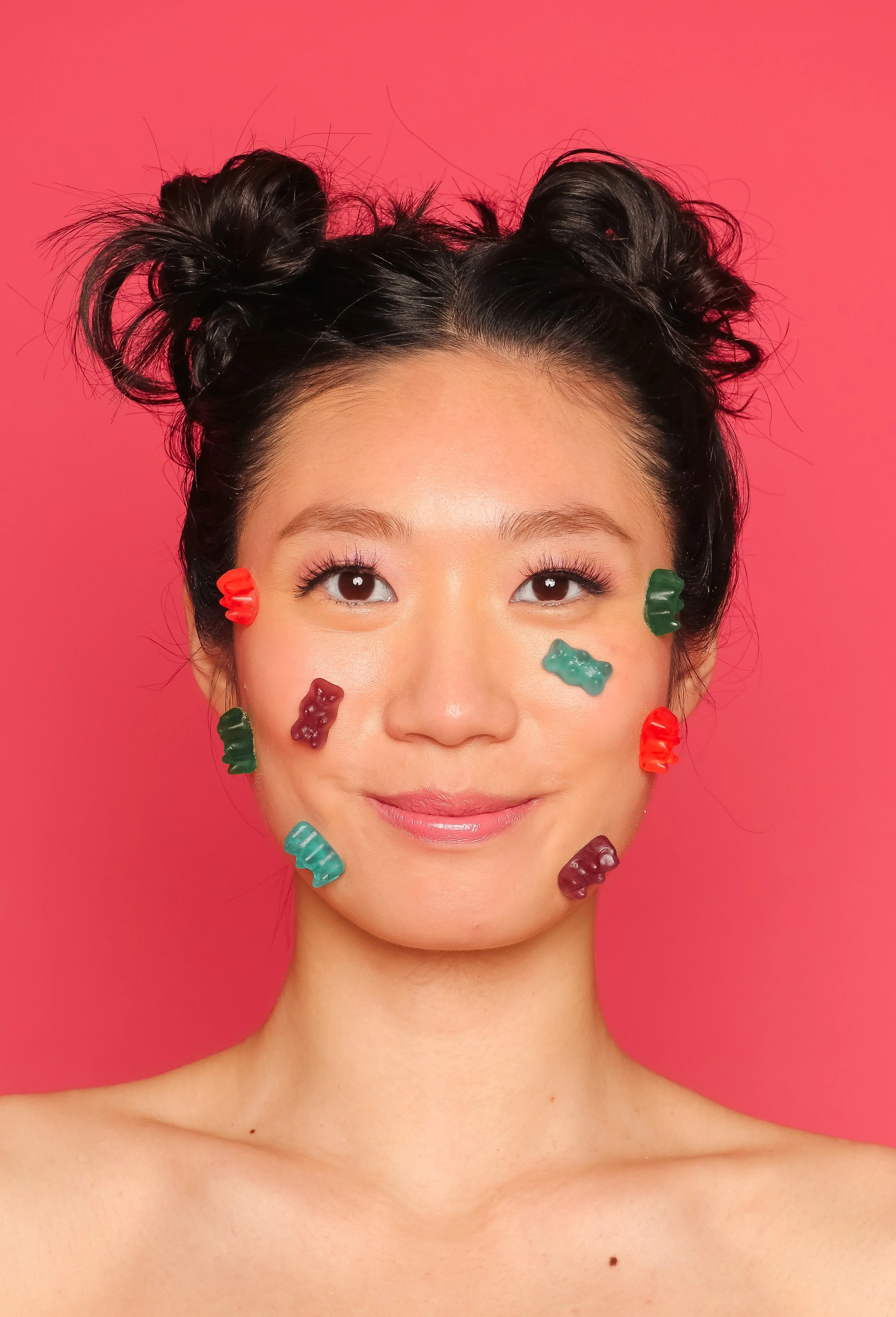 gummy bears on face of young woman and space buns hairstyle with a pink background