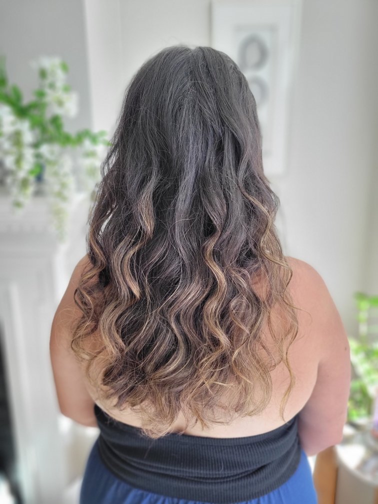 Woman with long, curly hair viewed from the back in a room with plants.