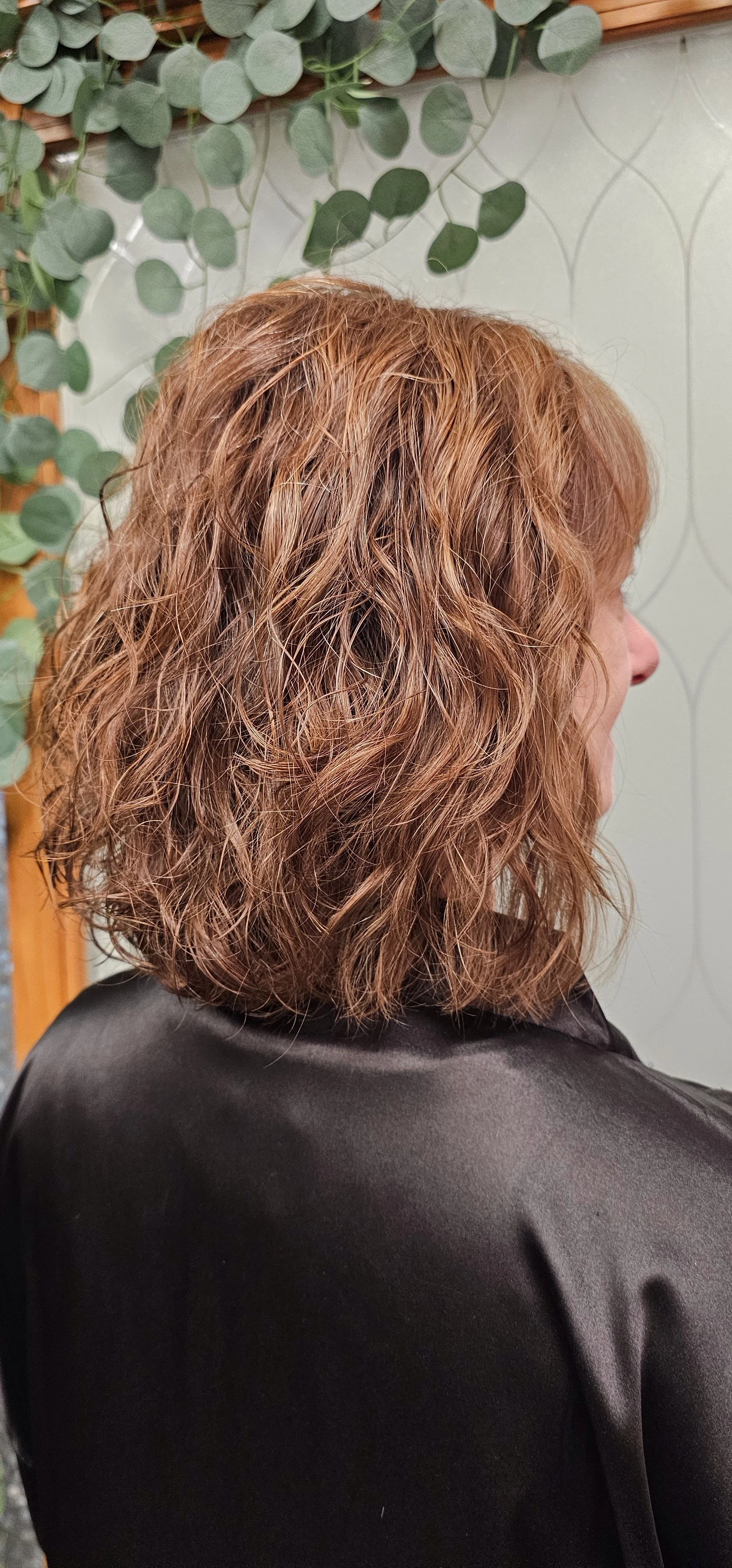 red haired woman with curly hair and green leaves near a window.