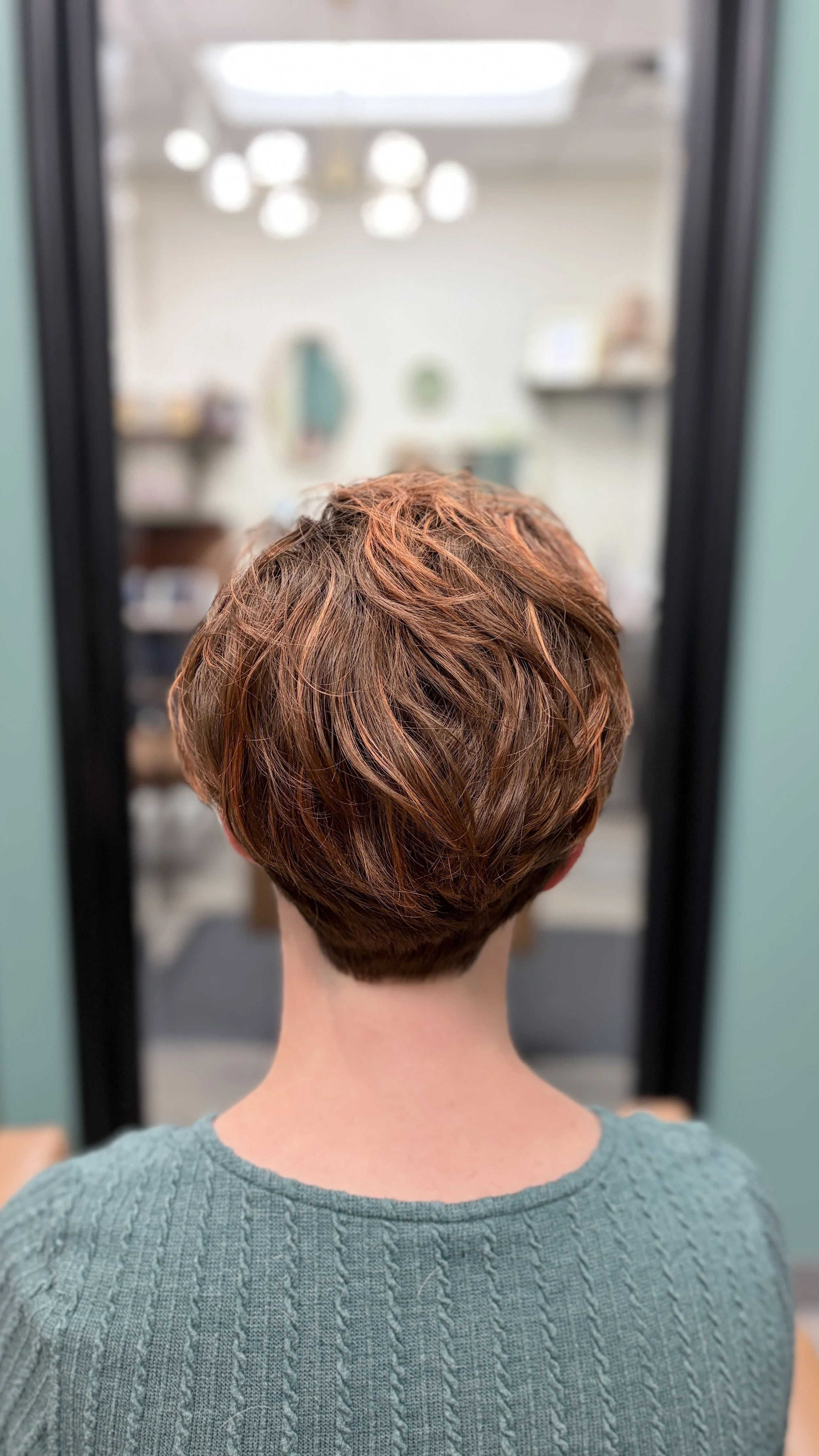 woman with short hair and copper highlights while wearing a green sage shirt