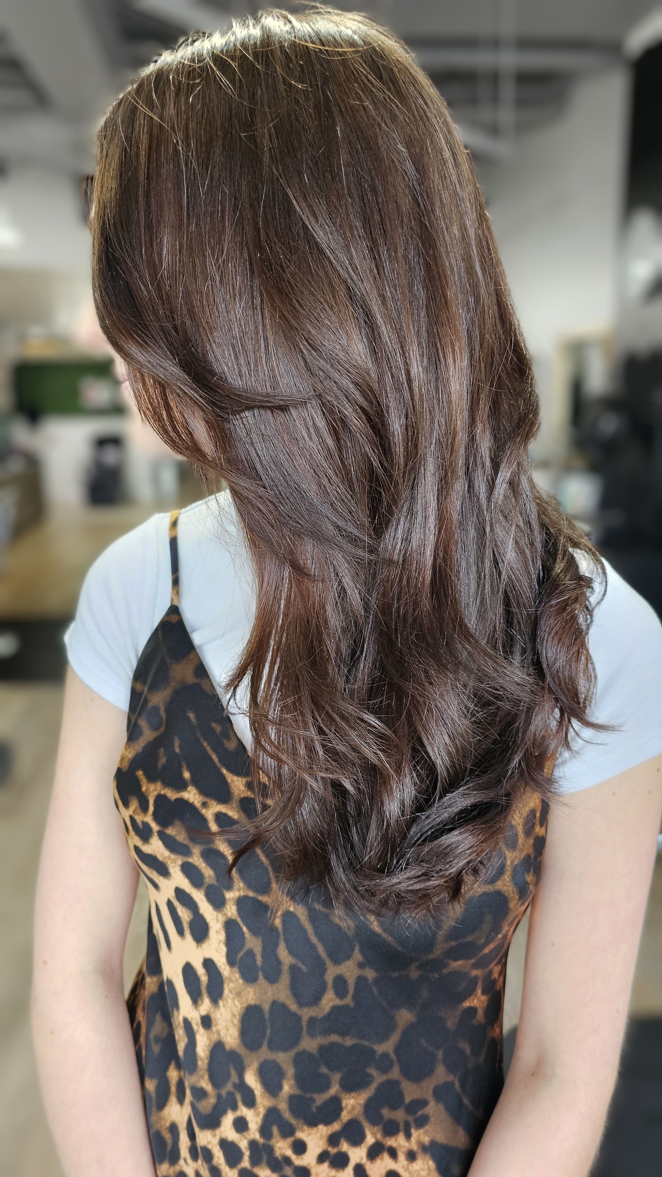 Woman with long brown hair in a leopard print dress, back view.