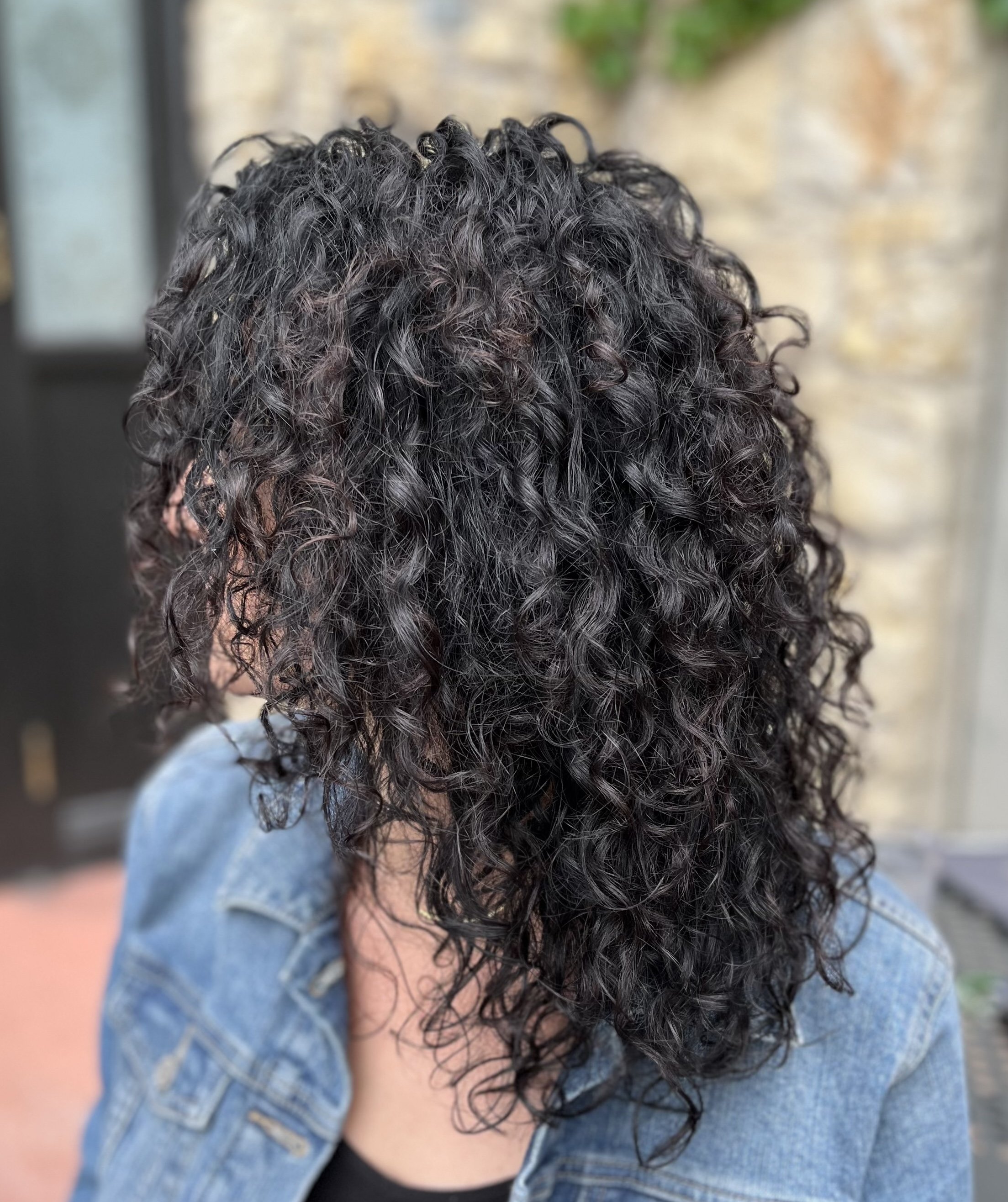 Person with curly dark hair wearing a denim jacket.