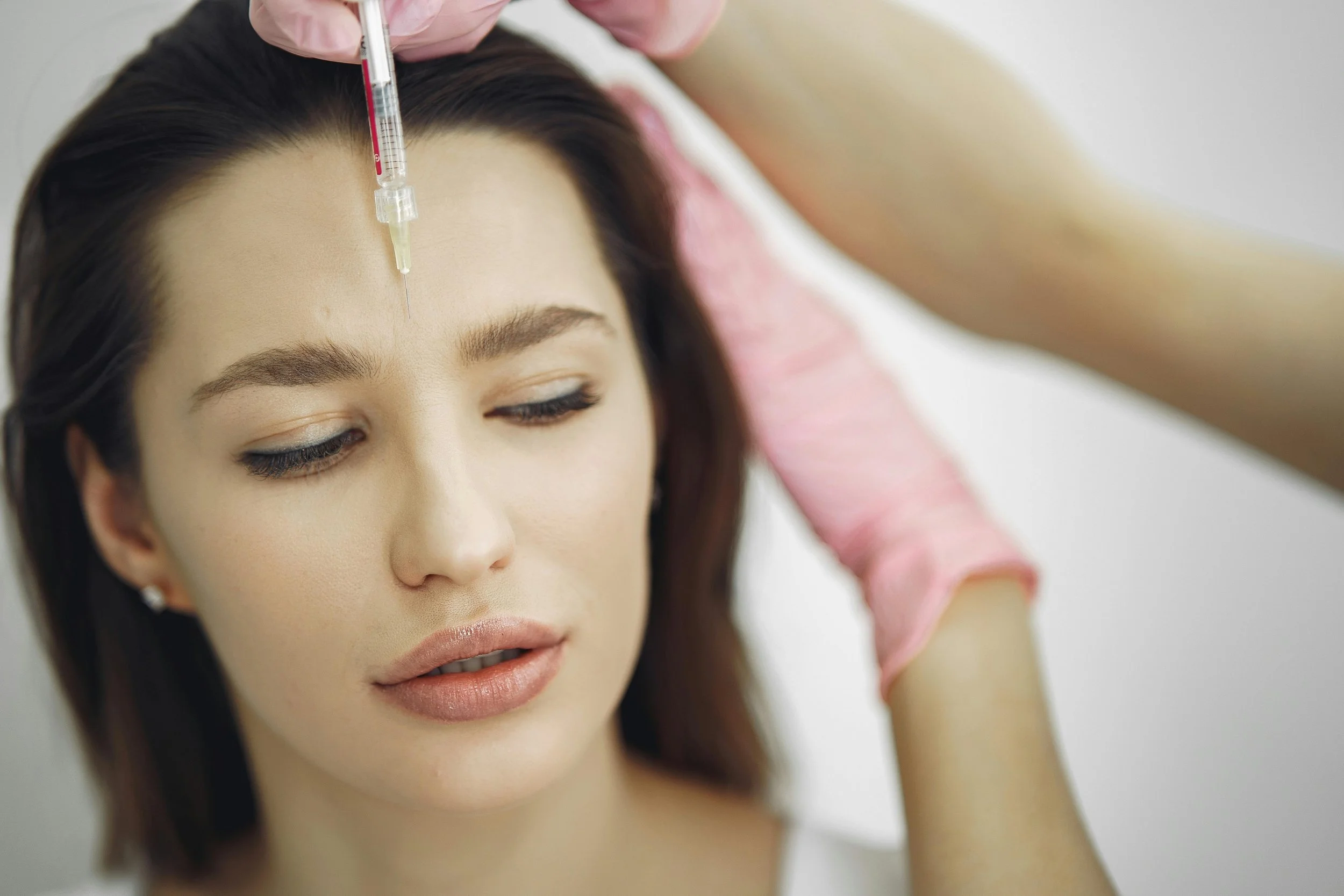 Woman receiving a cosmetic injection in her forehead by a medical professional