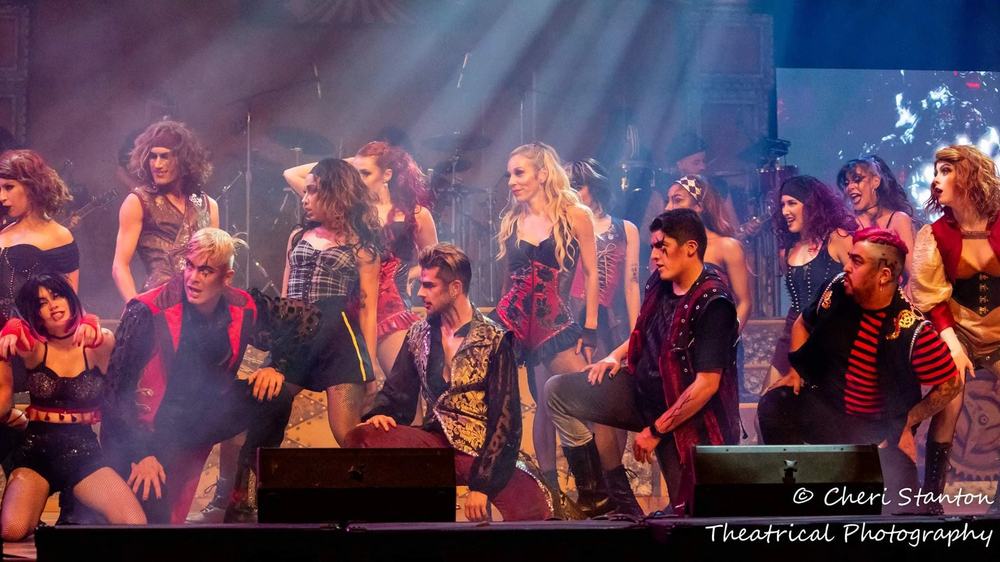 The full ensemble cast in dark gothic and rocker costumes gathers on stage under dramatic blue lighting for the finale of Dr. Diabolical's Monster Mash Bash