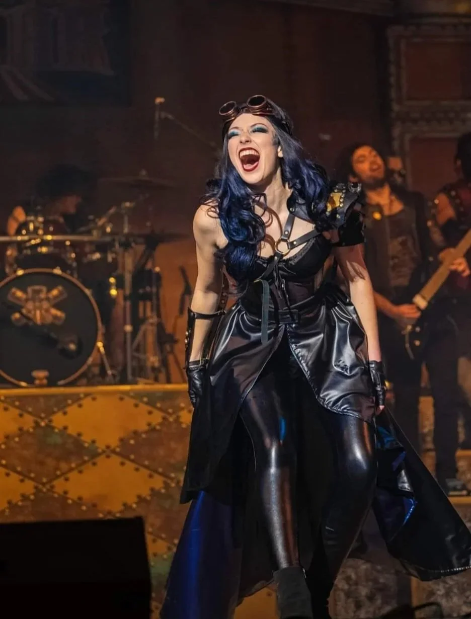 A performer in a dark dramatic gothic gown with flowing sleeves sings on stage for Dr. Diabolical's Monster Mash Bash