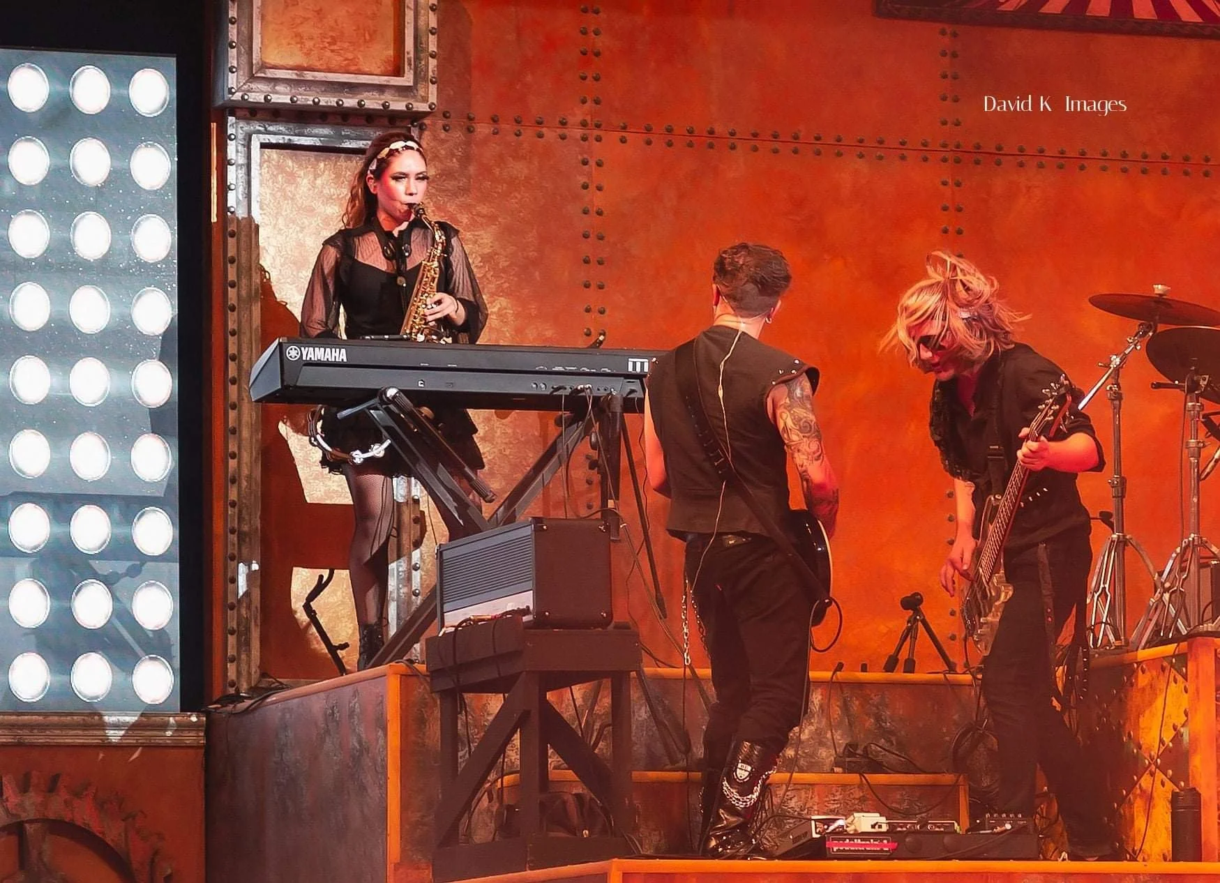 Performers in dark stage costumes play keyboard and guitar on stage under warm orange lighting for Dr. Diabolical's Monster Mash Bash