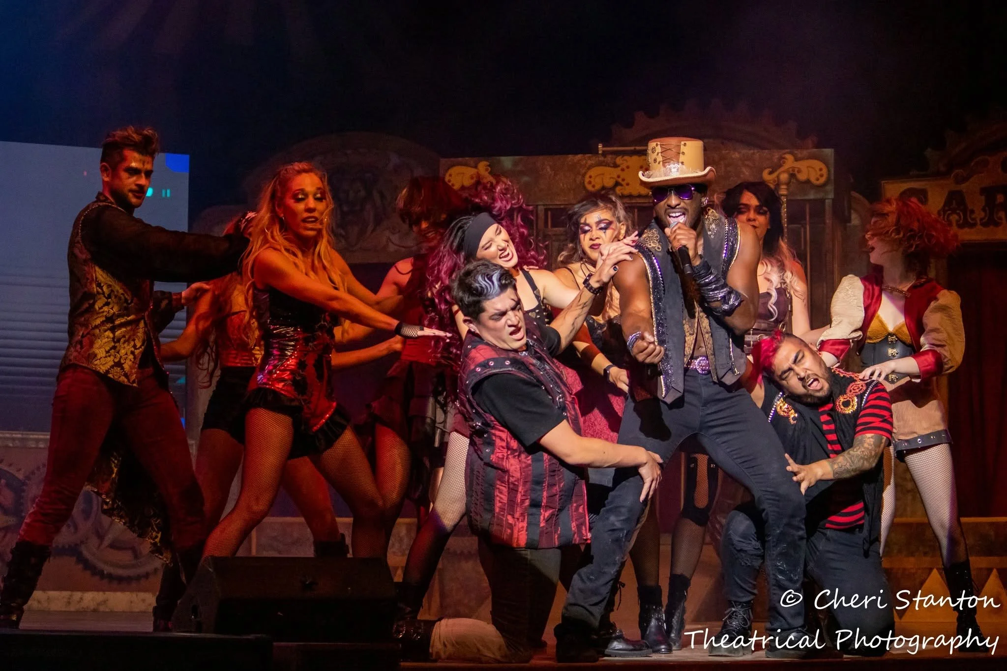 An ensemble cast in gothic Halloween performance costumes with distressed textures and dark colors performs on stage for Six Flags' Dr. Diabolical's Monster Mash Bash