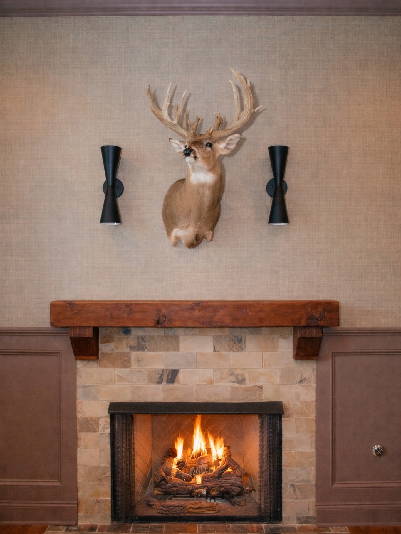The cozy vibe of this fireplace has us ready for Winter! ❄️ If you have a woodsman in your life and can&rsquo;t quite figure out how to make his memories fit in with your aesthetics, there is a way!  We added textured wallpaper, handsome light sconce