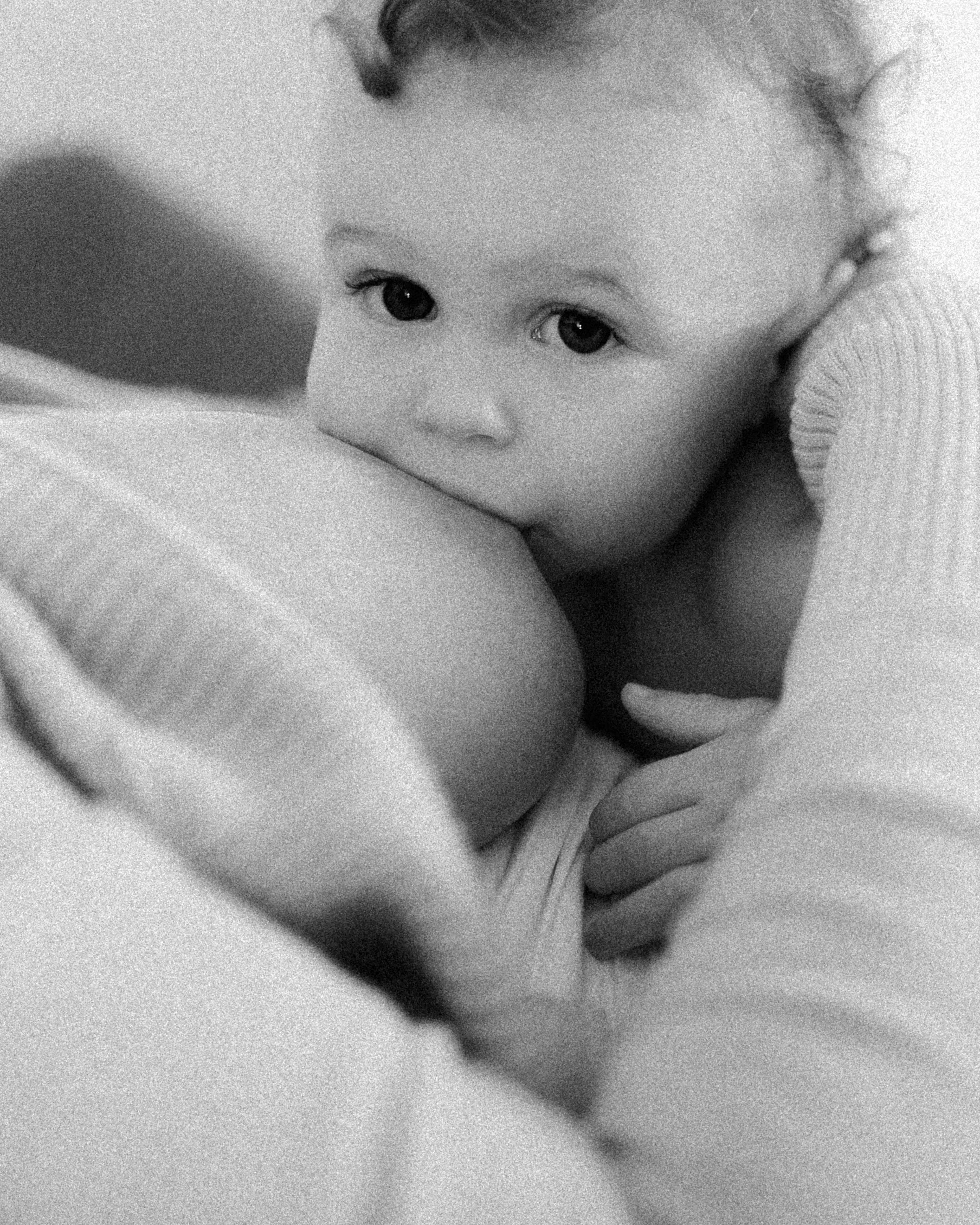 Close-up black and white photo of a young child with curly hair nursing wide eyes and a gentle expression.