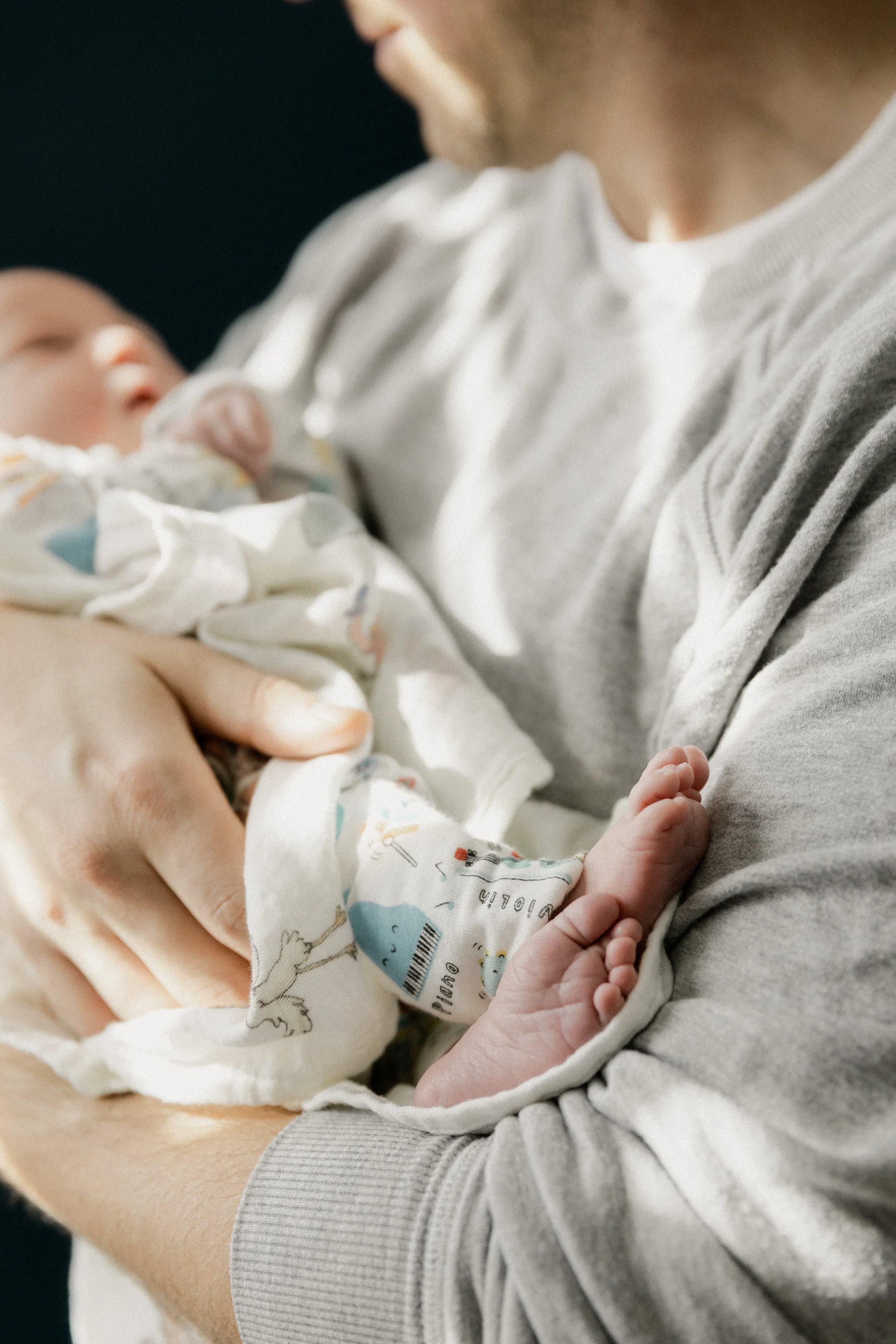 Person holding a newborn baby in their arms, with the baby wearing a hospital blanket and a hospital wristband.