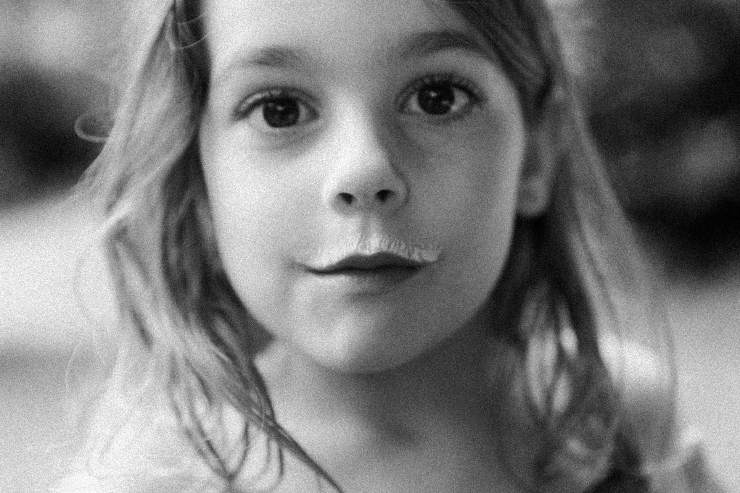 Black and white close-up photo of a young woman's face with visible eyes, eyebrows, nose, and lips, and wavy hair partially covering one side.
