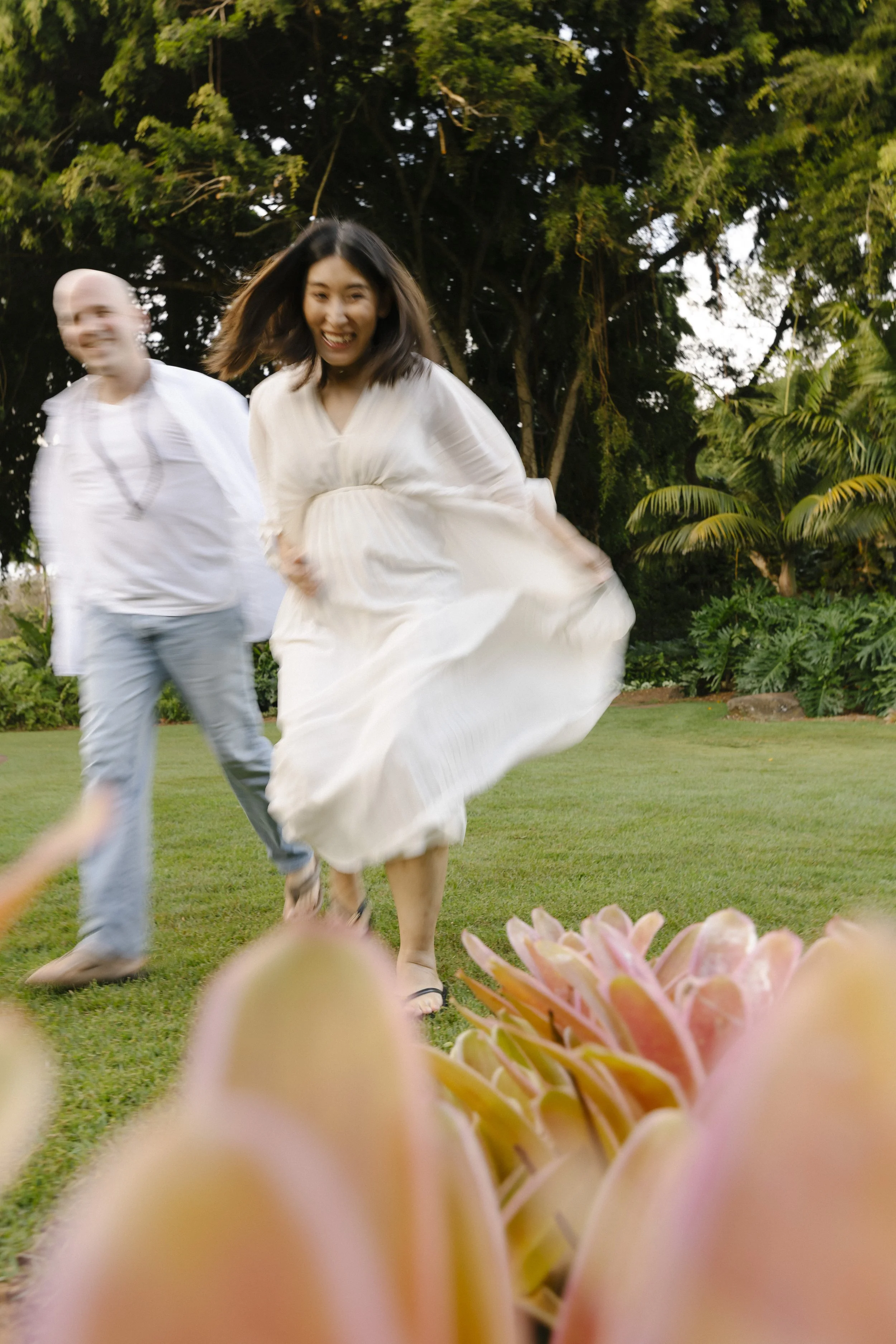 couple run in the grass during their maternity photos in Hawaii
