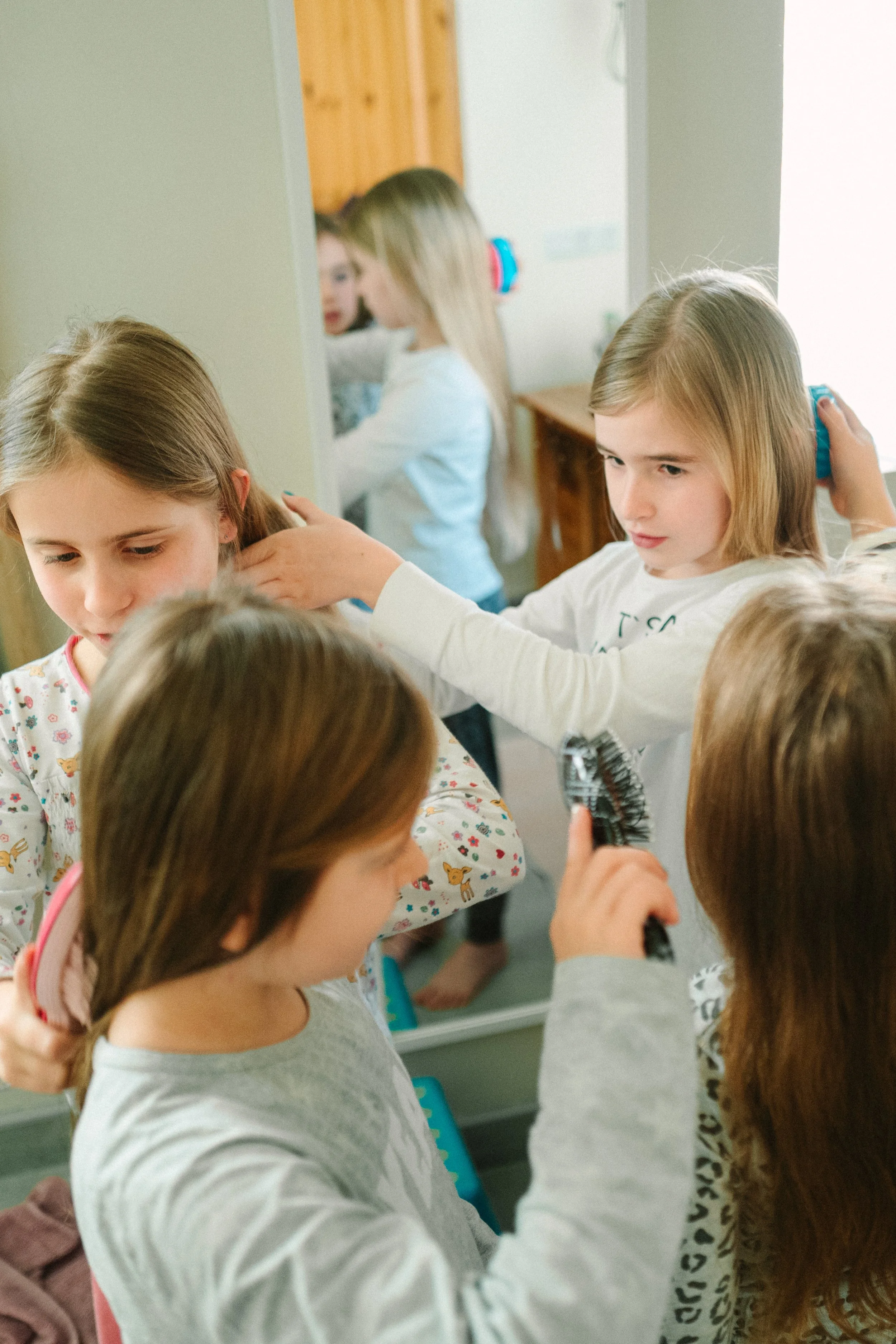 Children in a hair salon getting their hair brushed and styled, with a mirror reflecting their faces.