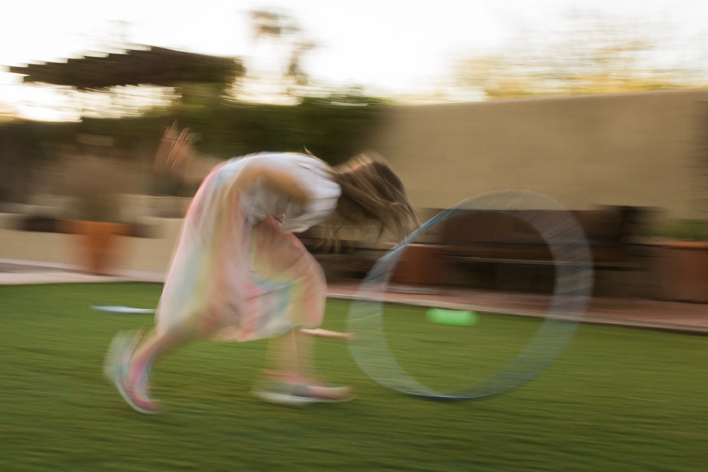 A person in a pastel tie-dye dress is running with a hula hoop, with a blurry background indicating motion or the photo was taken while moving.