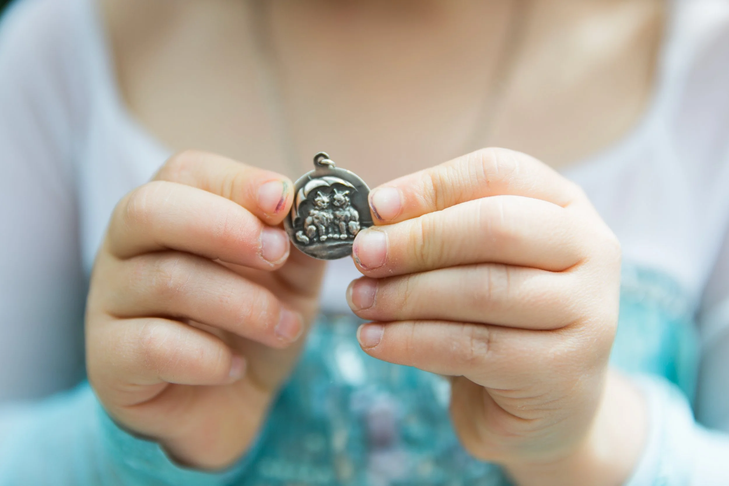 Close-up of a child's hand holding a small metal charm with a cat design.