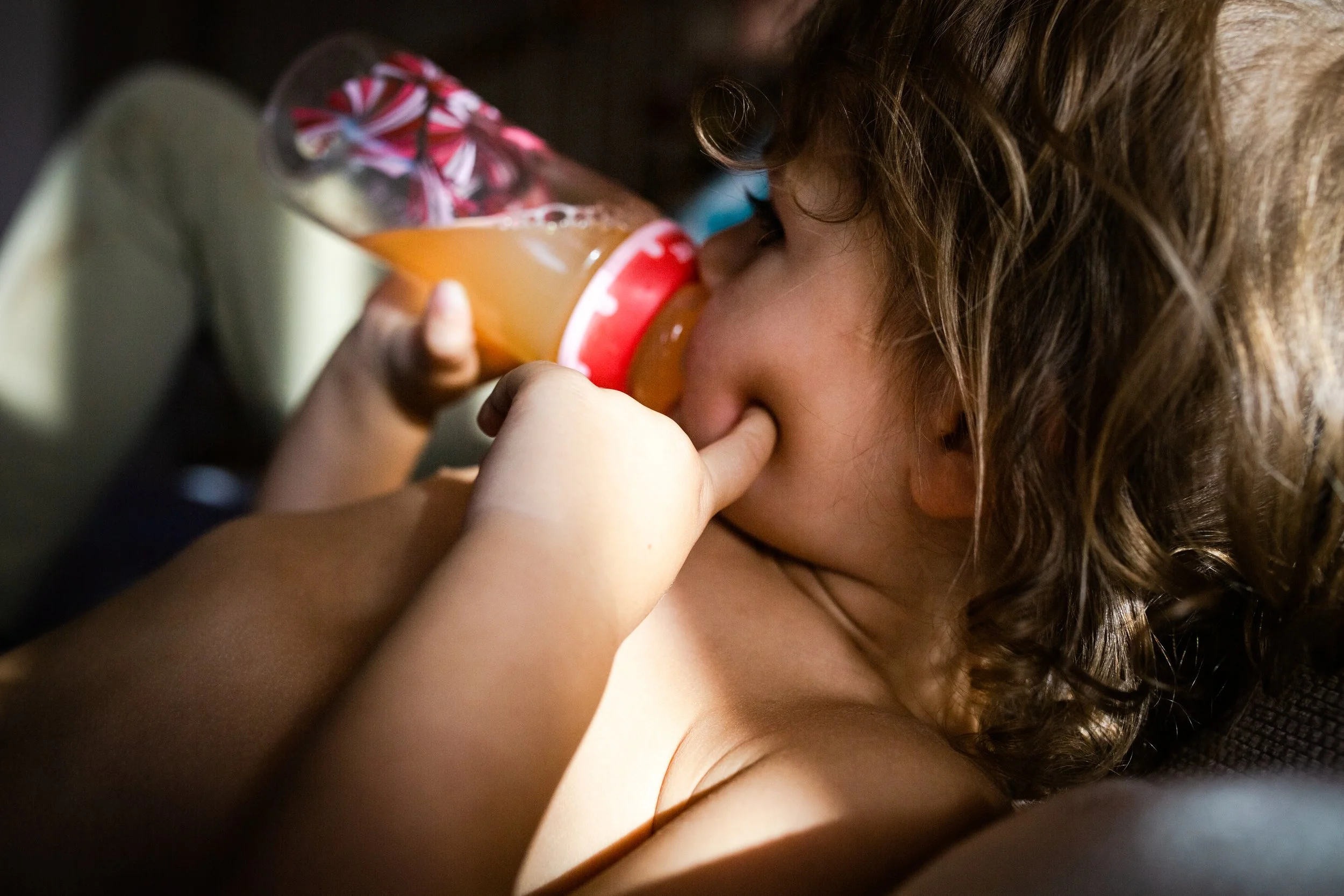 A young child with curly hair drinking from a bottle of orange juice.