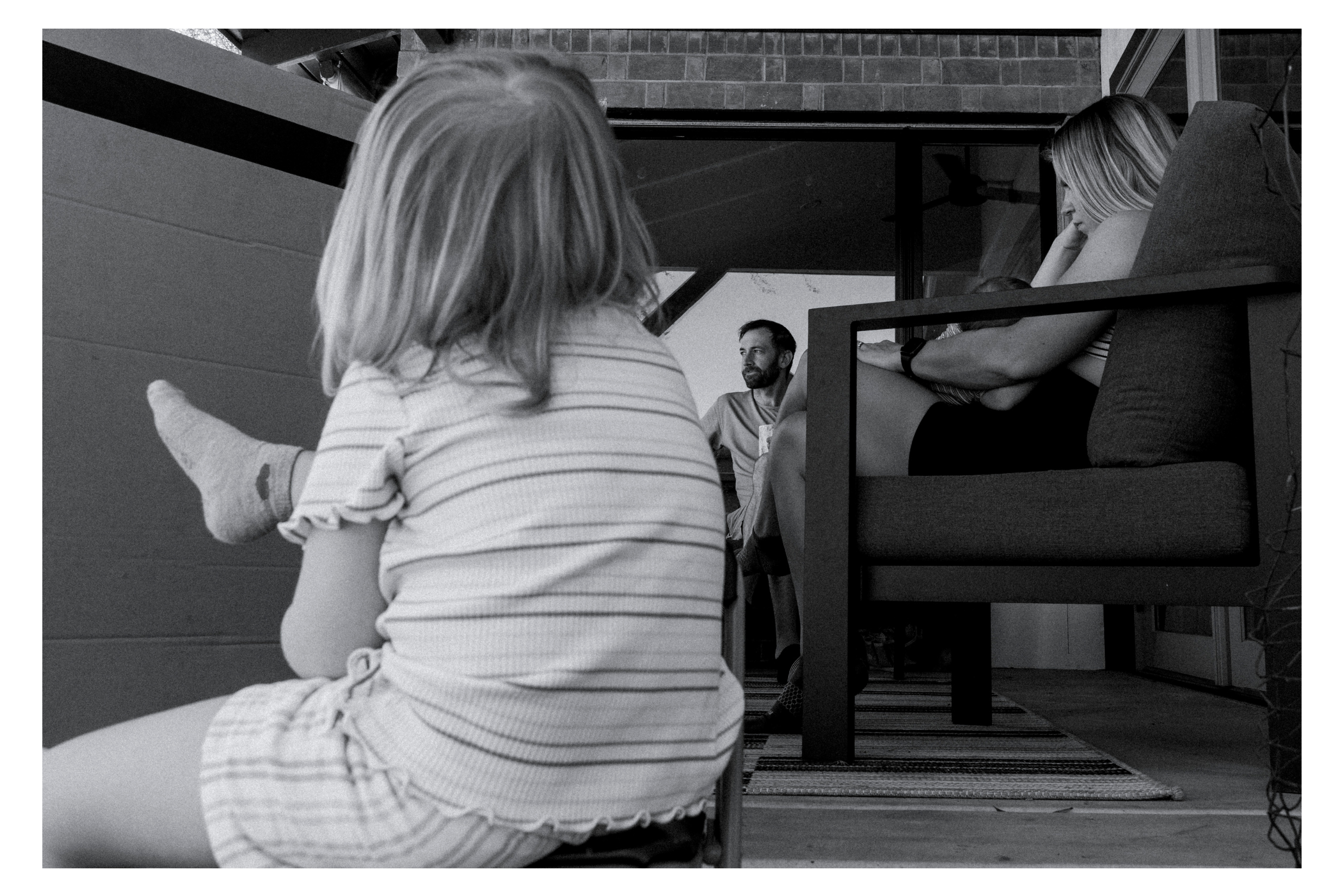 little girl casually rests her foot on the back of a chair while her family relaxes on the porch tucson family session