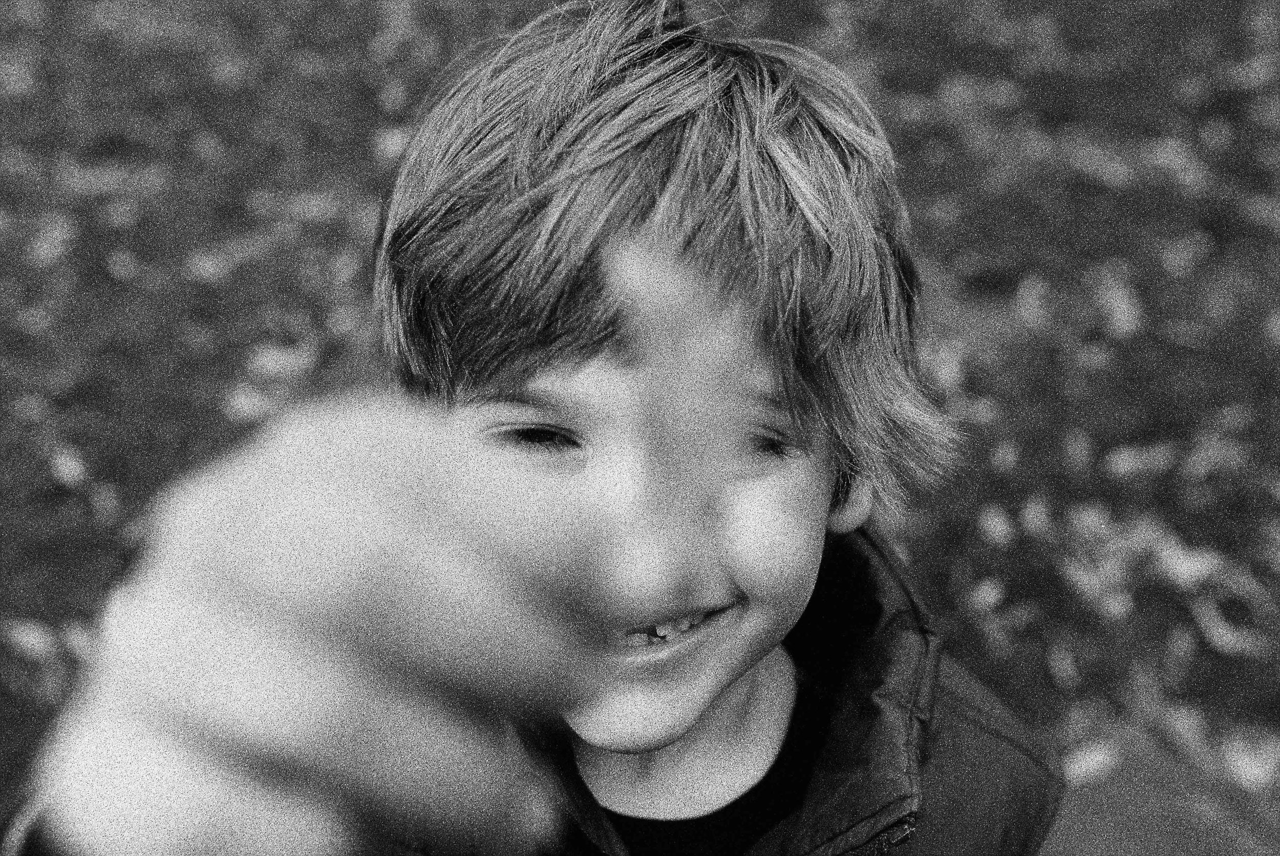 Black and white photo of a smiling child with tousled hair, making a playful gesture with their hand.
