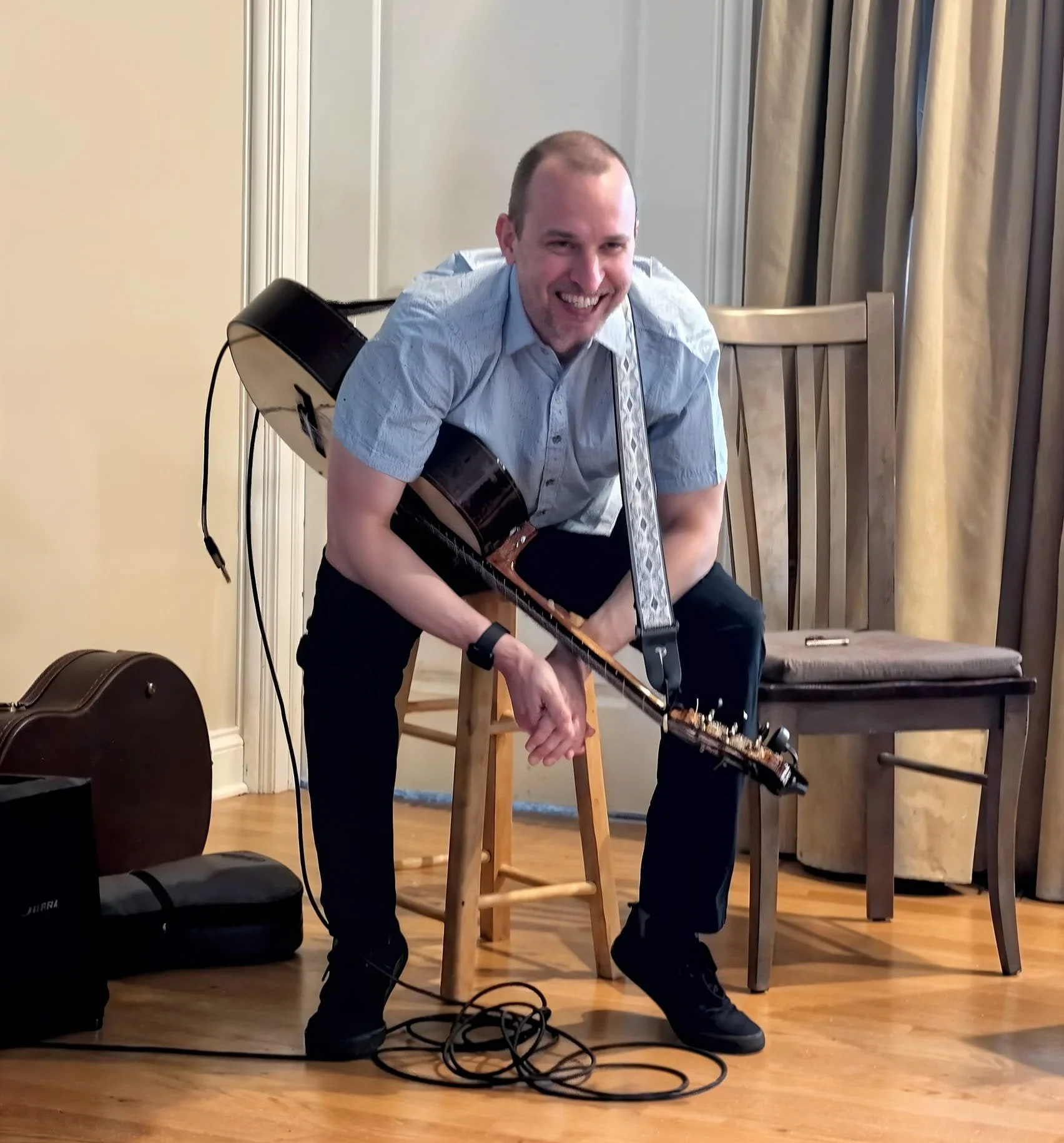 Jim Perona playing guitar in a warmly lit private event space