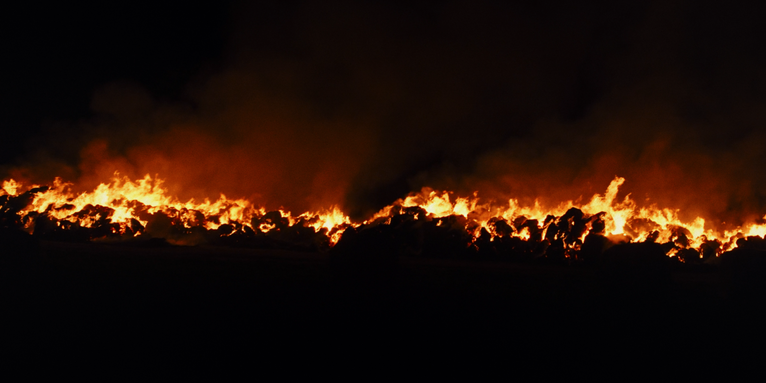 Nighttime scene of a large wildfire with flames and thick black smoke.