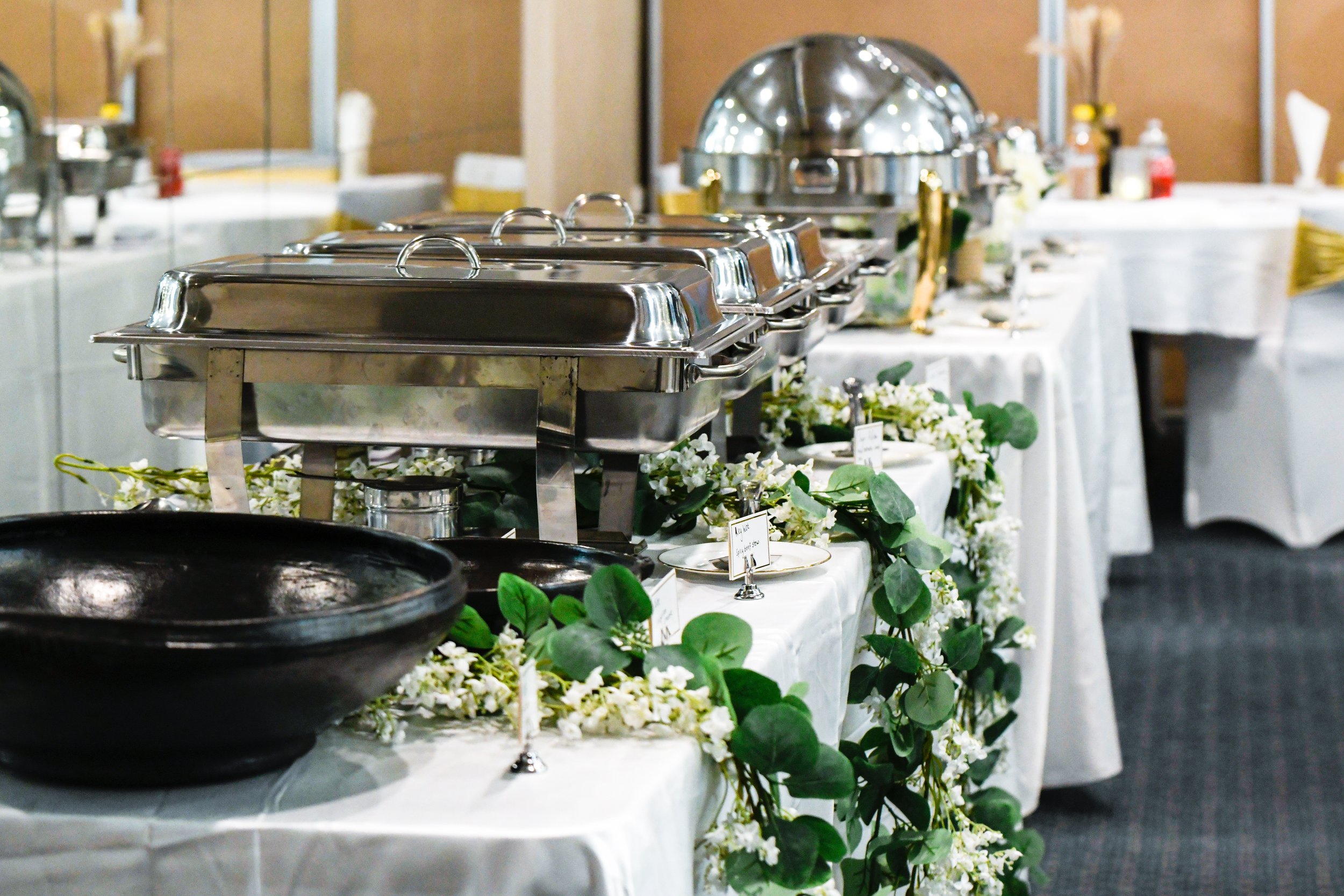 Buffet setup with chafing dishes on a table decorated with white flowers and greenery.