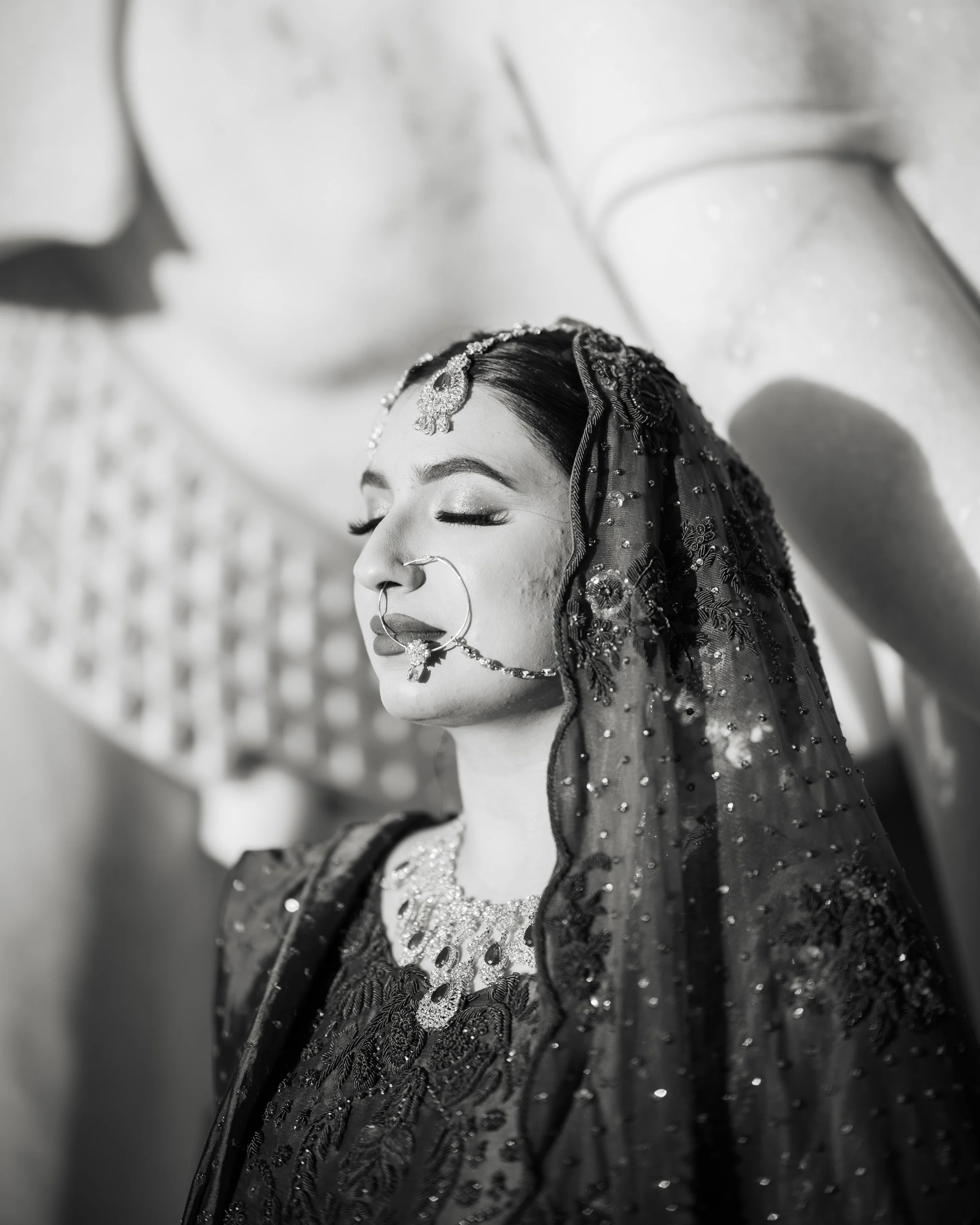 A woman dressed in traditional Indian attire, wearing jewelry and a decorative veil, with her eyes closed, appears to be meditating or in a moment of serenity.