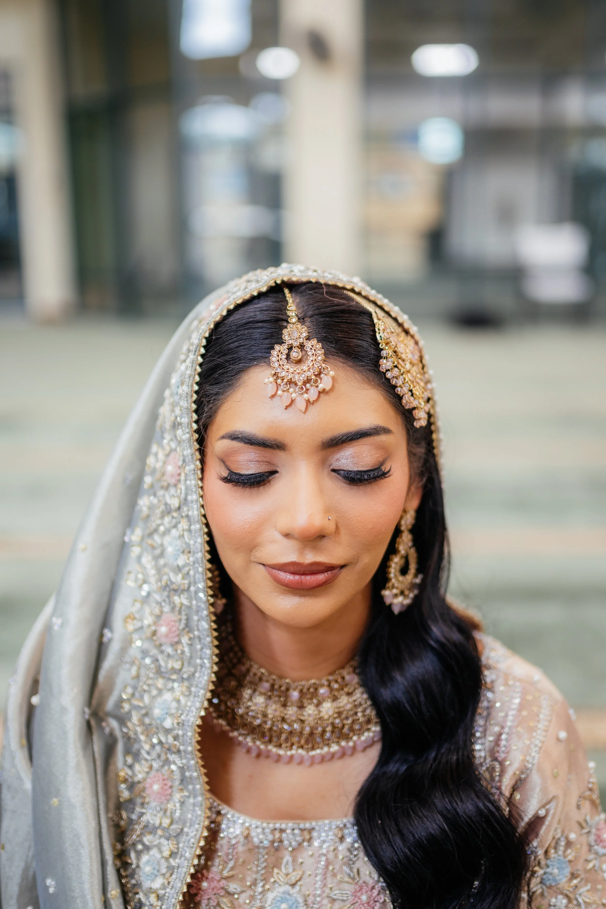 Close-up of a woman wearing traditional South Asian bridal attire with ornate jewelry, including a maang tikka, earrings, and necklace, with her eyes closed and a soft smile.