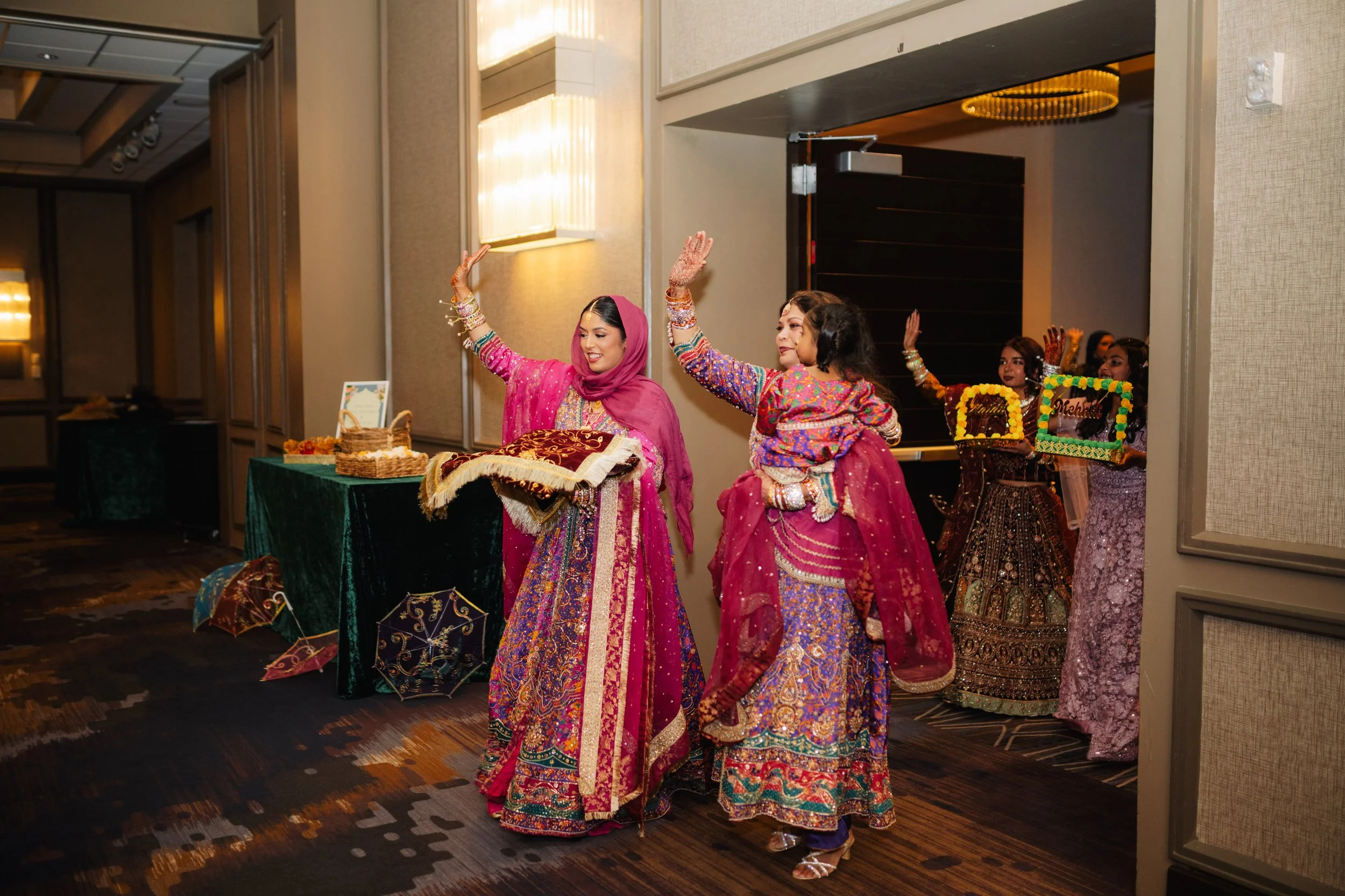 Women dressed in traditional colorful South Asian attire dancing at an indoor celebration or party.