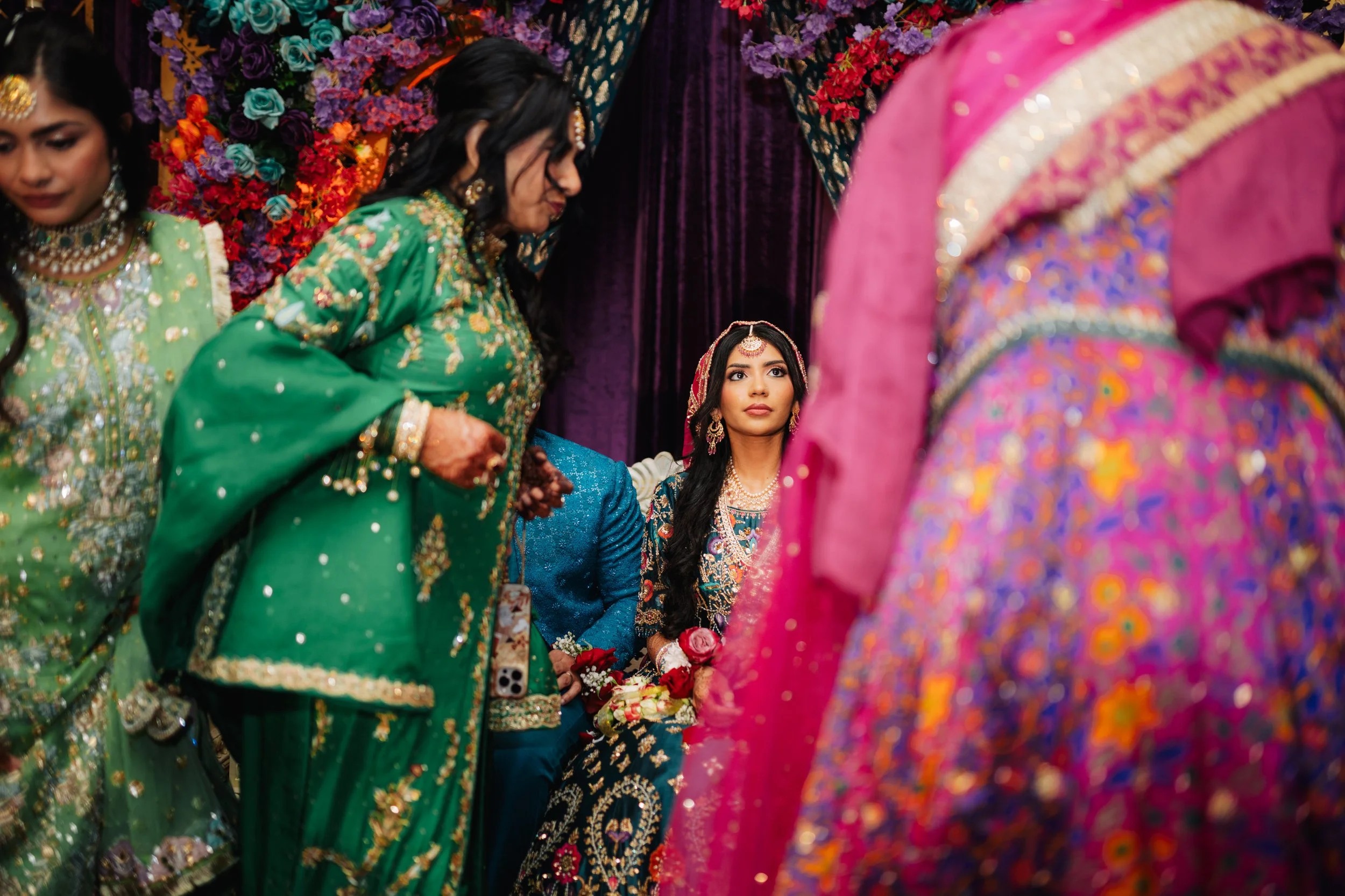 Women dressed in colorful traditional Indian attire, participating in a cultural celebration with flowers and vibrant decorations.