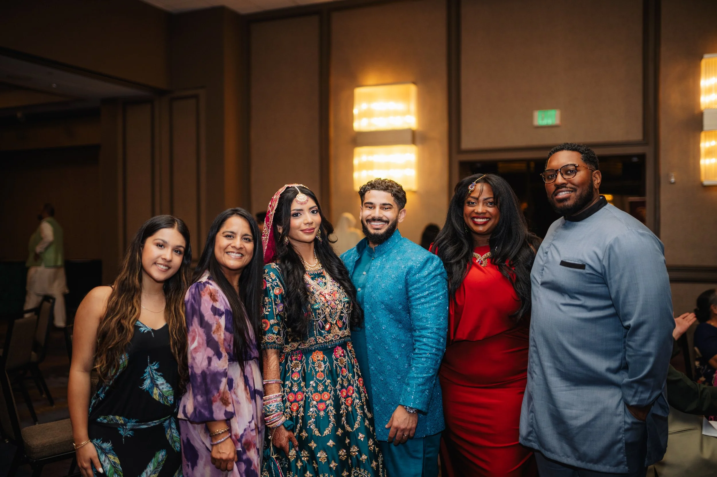 Group of six people dressed in colorful clothing, posing for a photo indoors at a social event.