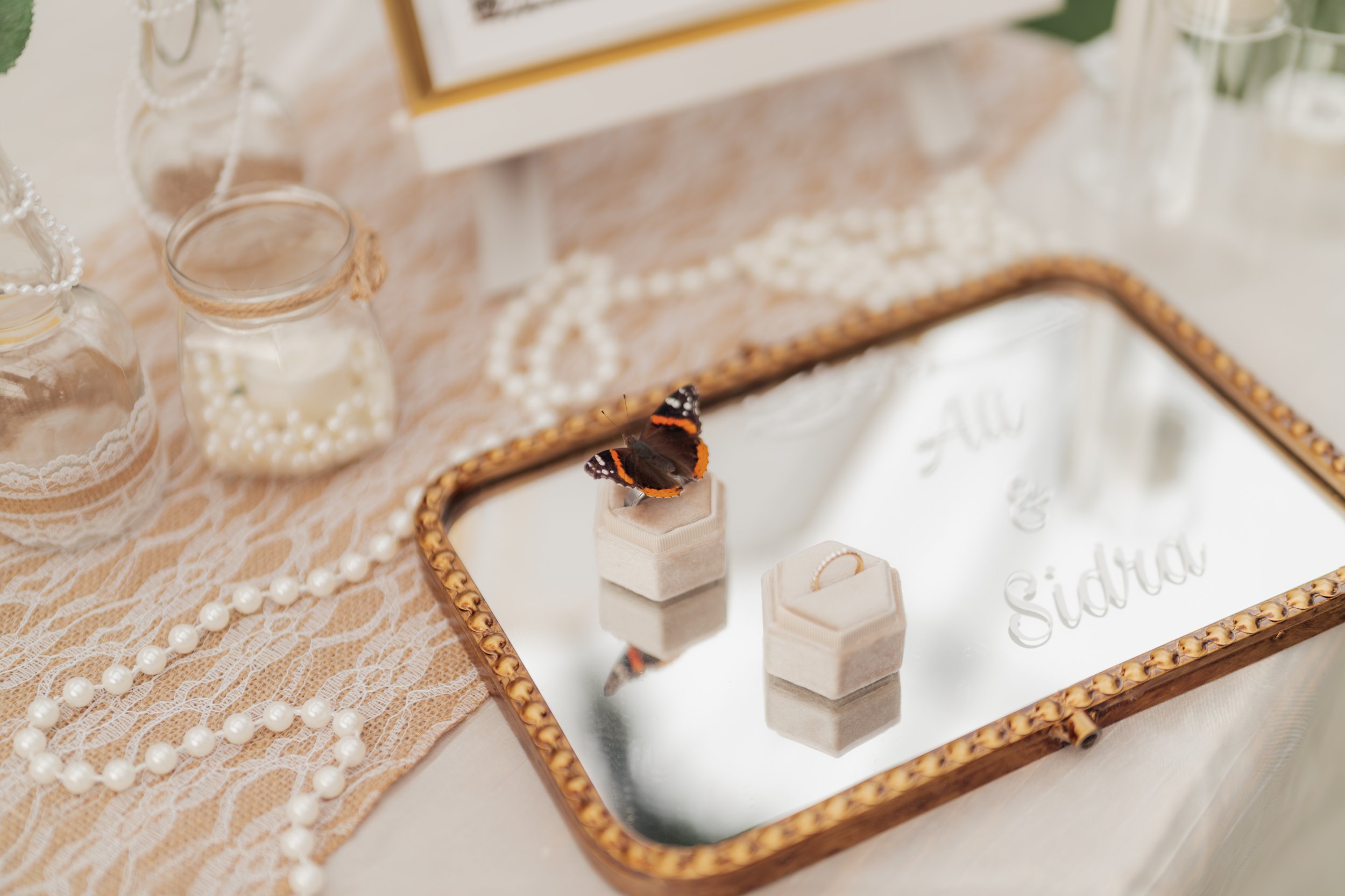 Close-up of a jewelry display with pearl necklaces, a butterfly decoration, and a ring, set on a lace tablecloth.