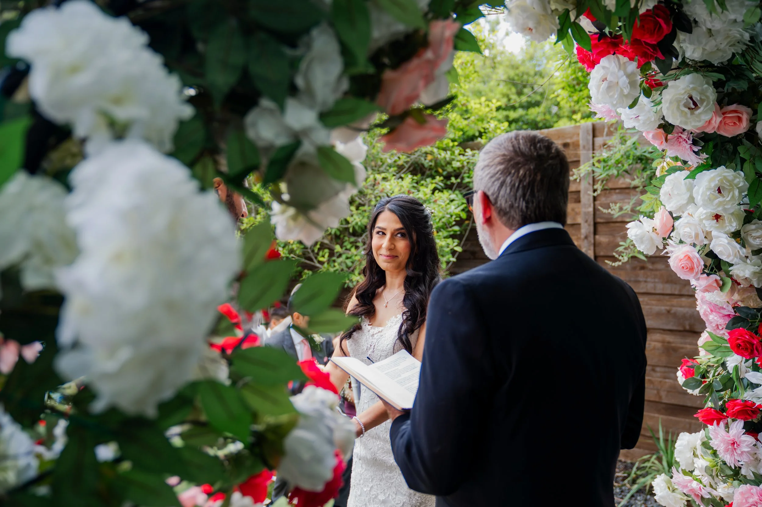 A bride and groom exchanging vows during their outdoor wedding ceremony, surrounded by colorful flowers and greenery.